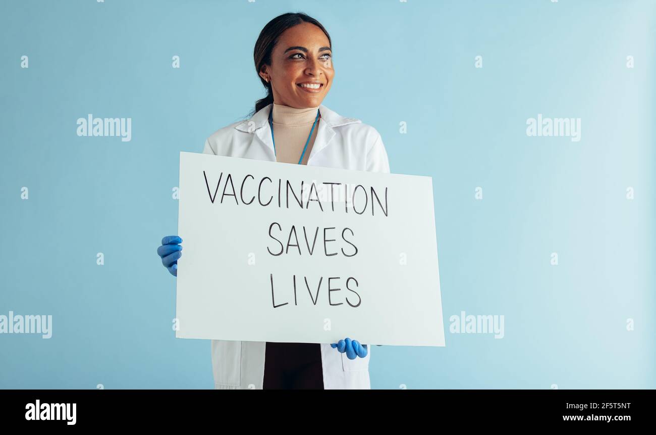 La vaccinazione salva il banner delle vite nelle mani di una donna che si occupa di assistenza sanitaria. Medico che guarda via e sorridendo con la carta slogan di consapevolezza della vaccinazione in Foto Stock