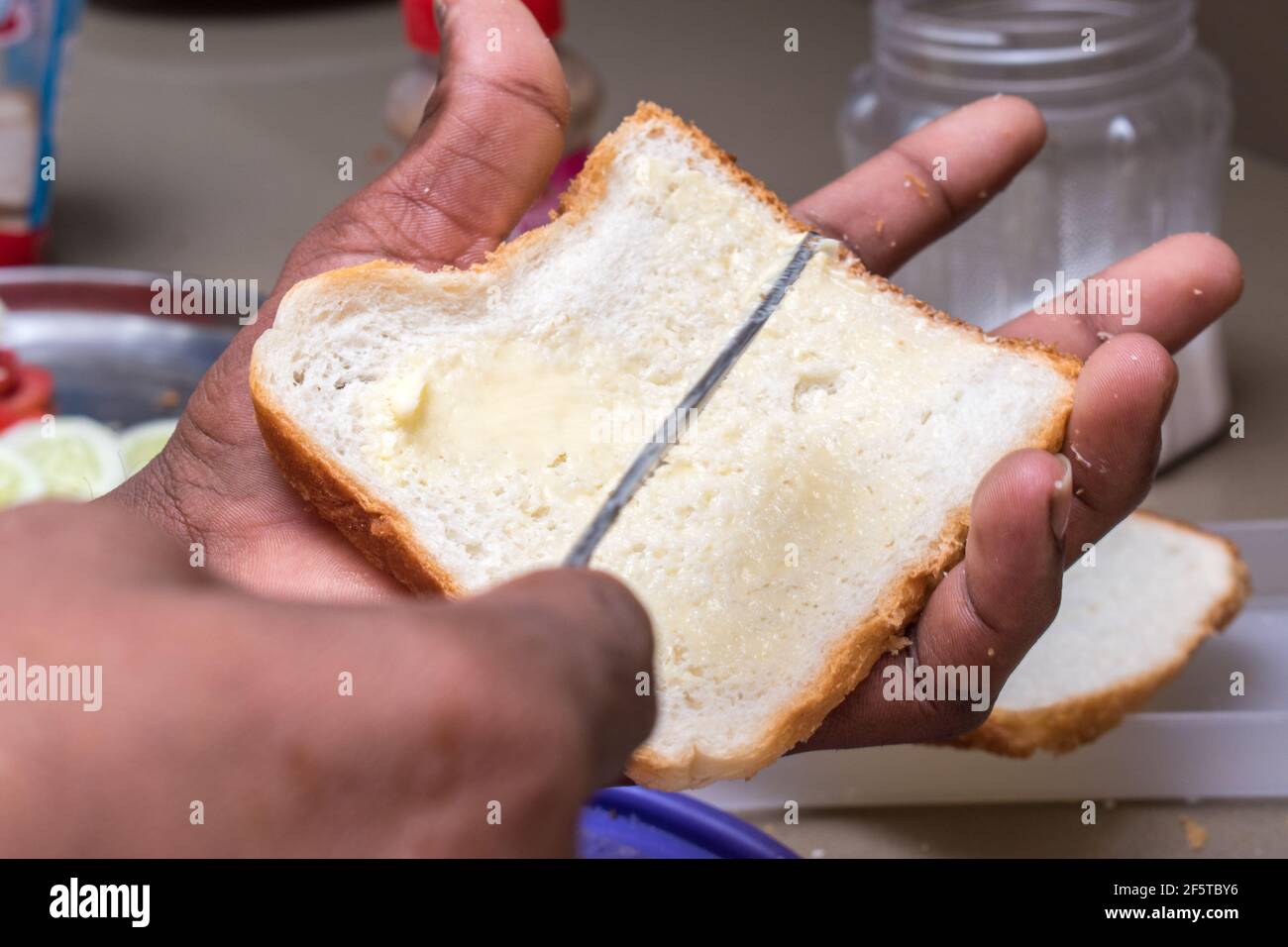 mani che applicano il burro sul pane bianco con il coltello per il burro Foto Stock