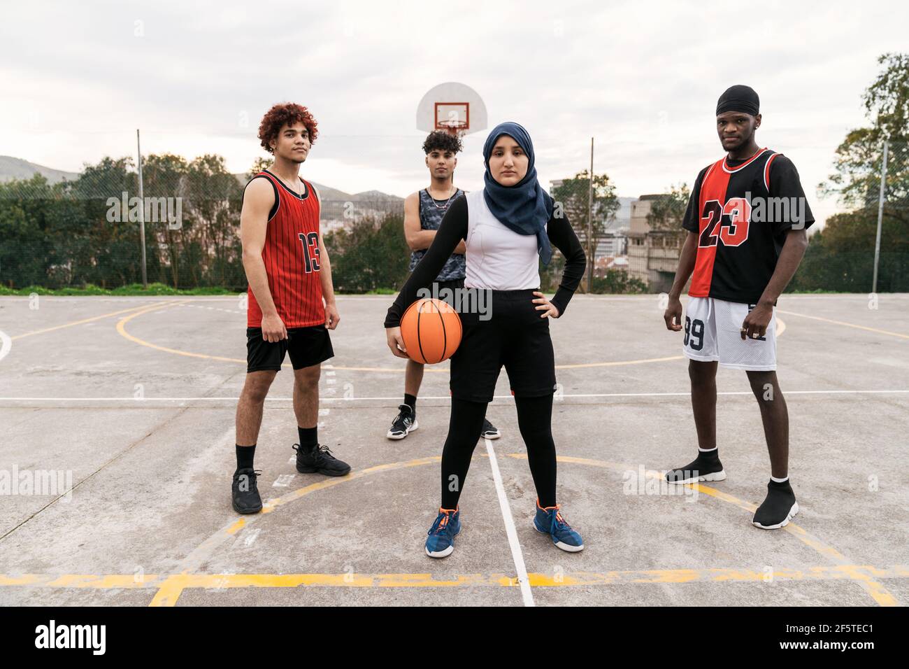 Squadra multietnica di streetball con palla in piedi sugli sport di pallacanestro terreno in città guardando cmaera Foto Stock