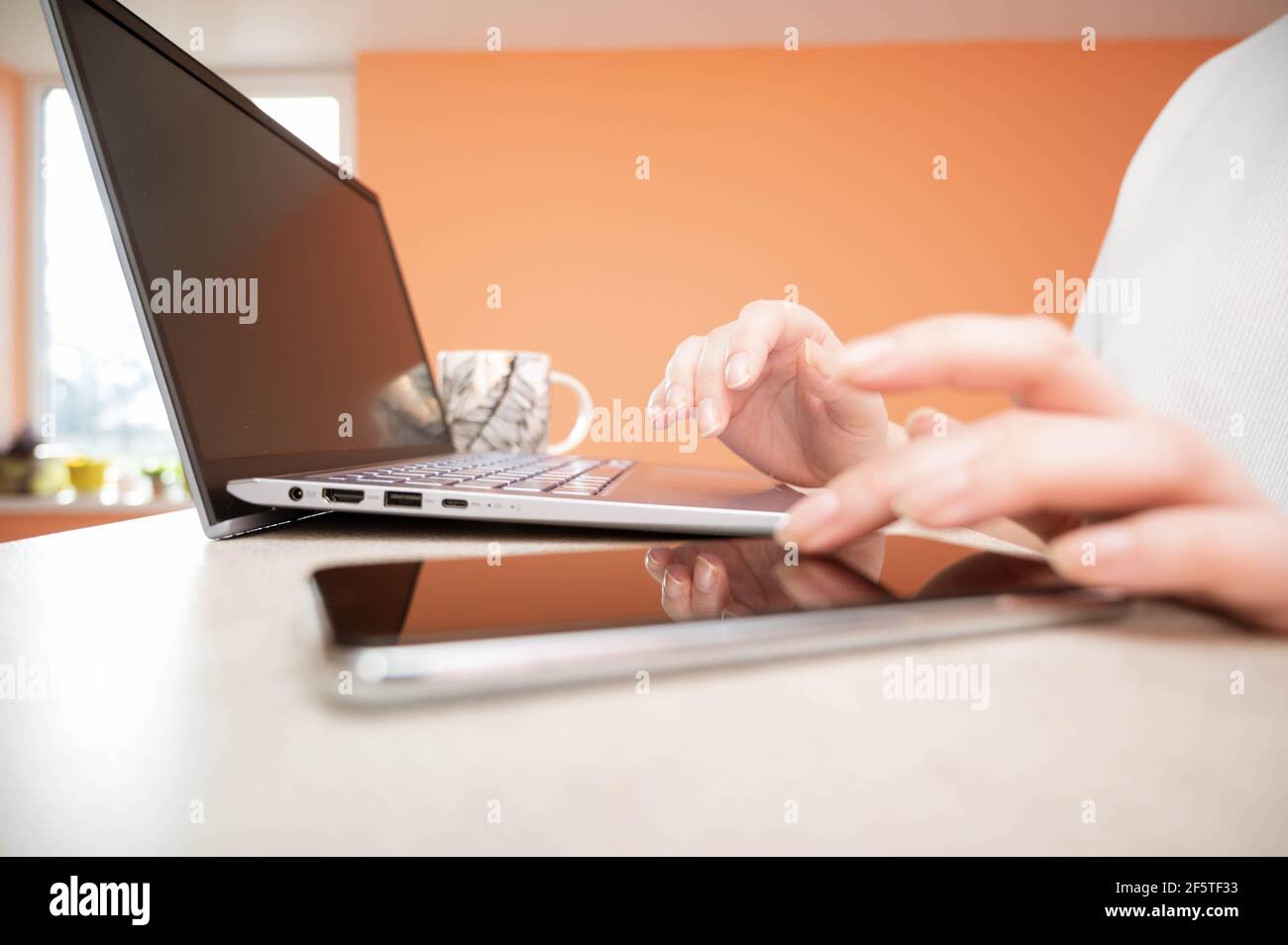 Donna che lavora su un computer portatile e utilizza il telefono. Multitasking, concetto di lavoro da casa. Foto Stock