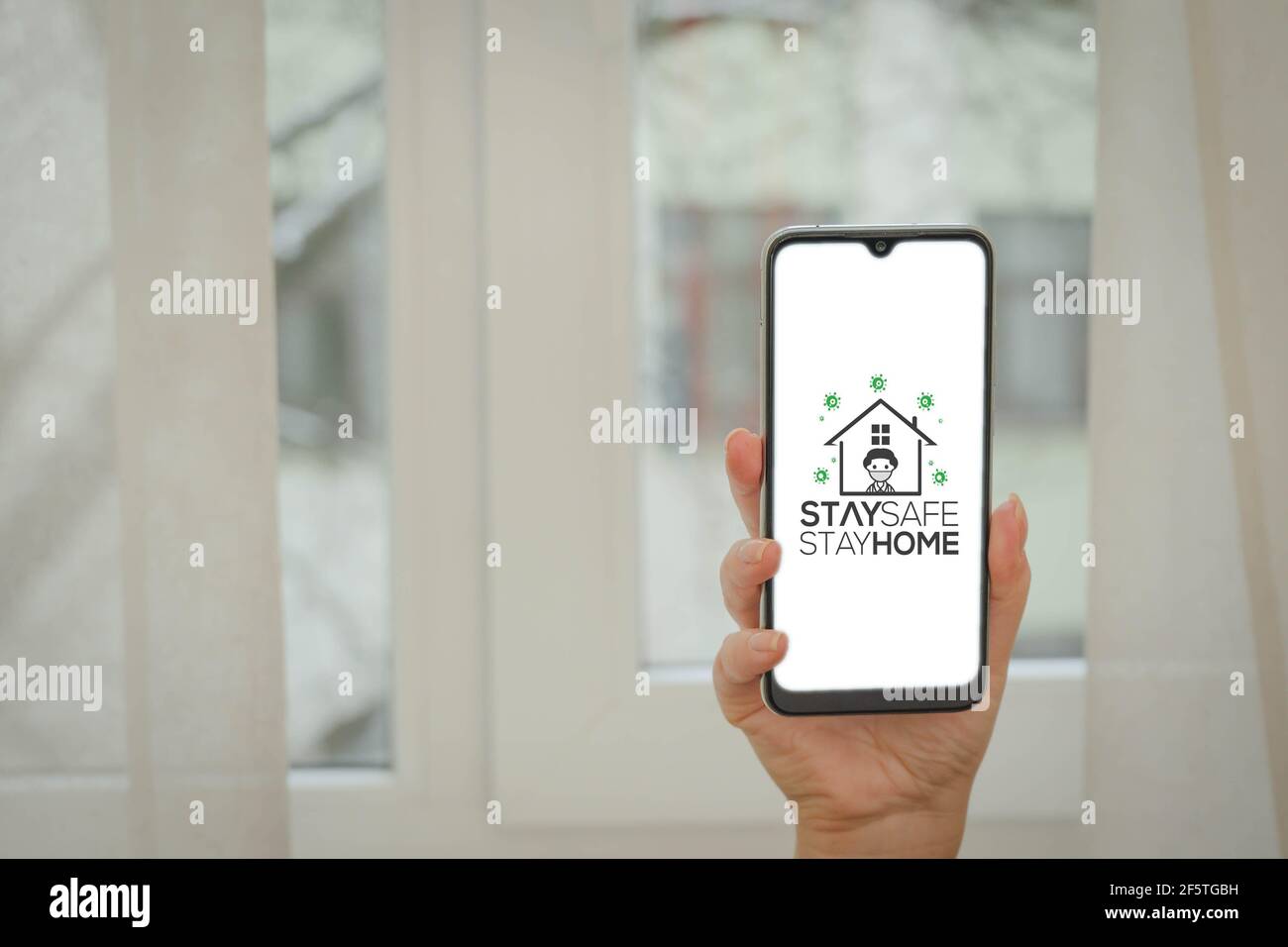 Telefono femminile con presa a mano e testo STAY SAFE STAY HOME. Rimani sicuro a casa durante il concetto di pandemia di coronavirus. Foto Stock