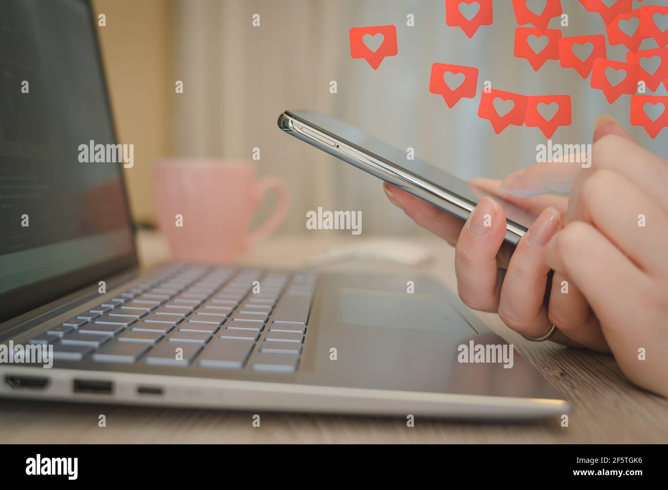 Donna che tiene in mano lo smartphone con l'icona del cuore nell'ufficio domestico. Concetto di tecnologia, business e stile di vita sociale. Foto Stock