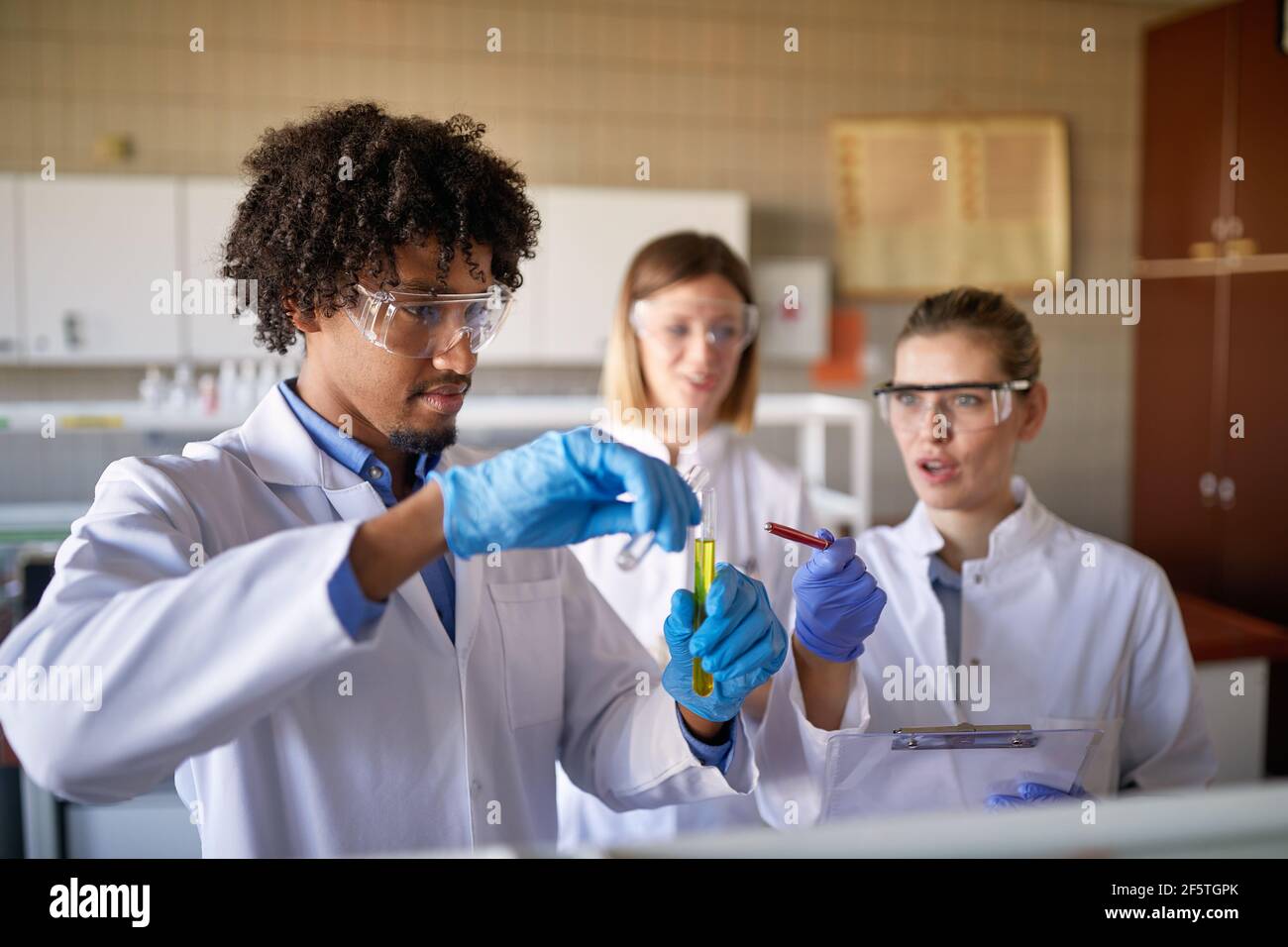 I giovani studenti di chimica in un equipaggiamento protettivo mescolano alcuni prodotti chimici nel laboratorio universitario in un'atmosfera di lavoro. Scienza, chimica, laboratorio, persone Foto Stock