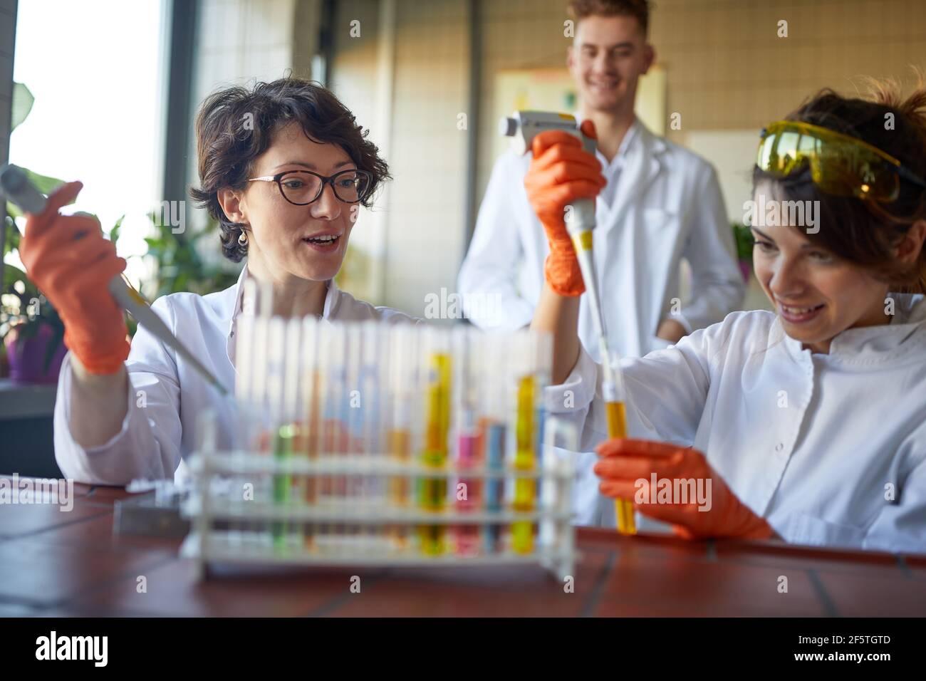 Le giovani donne apprezzano il pipettaggio dei prodotti chimici in un'atmosfera rilassata presso il laboratorio universitario. Scienza, chimica, laboratorio, persone Foto Stock
