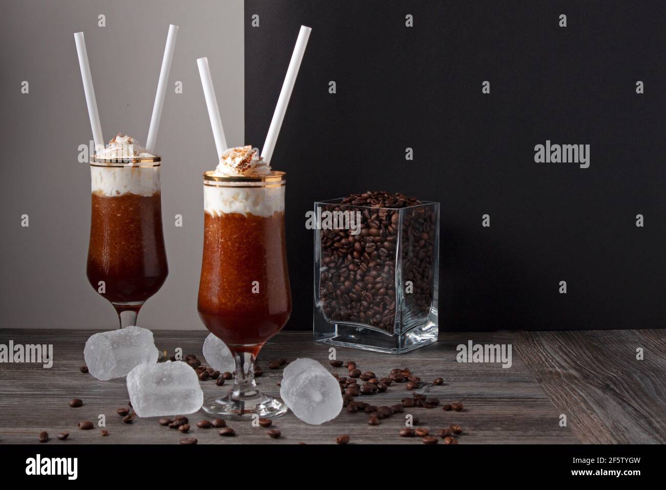 concetto di una vita still su due bicchieri di granita di caffè con panna, con ghiaccio e chicchi di caffè intorno ai bicchieri e un vaso di vetro pieno di chicchi di caffè Foto Stock