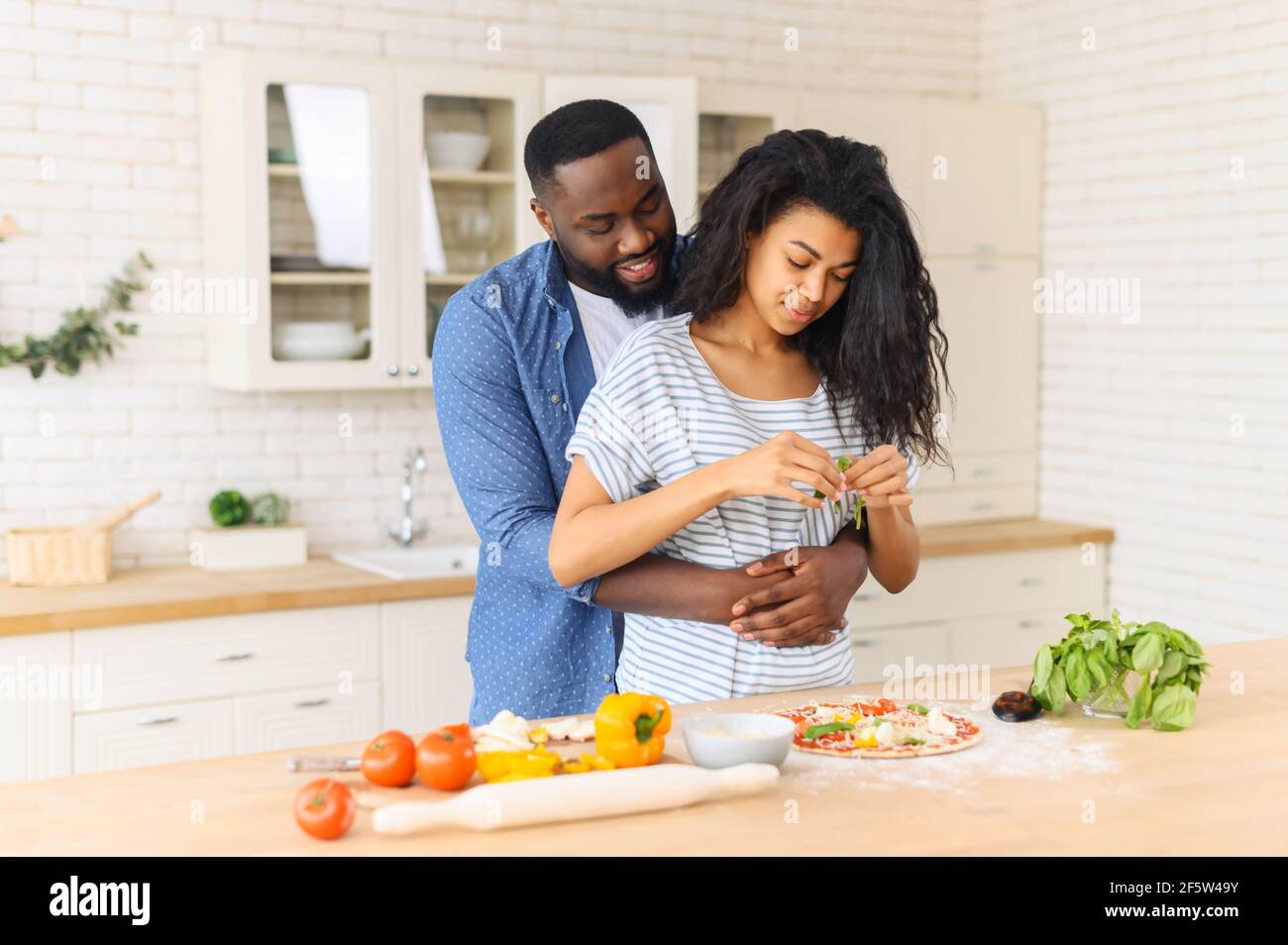 Il marito nero affettuoso abbraccia la moglie che prepara il suo cibo  preferito - pizza fatta in casa deliziosa, uomo affamato in attesa di un  gustoso pranzo yummy, guarda sua moglie decorare