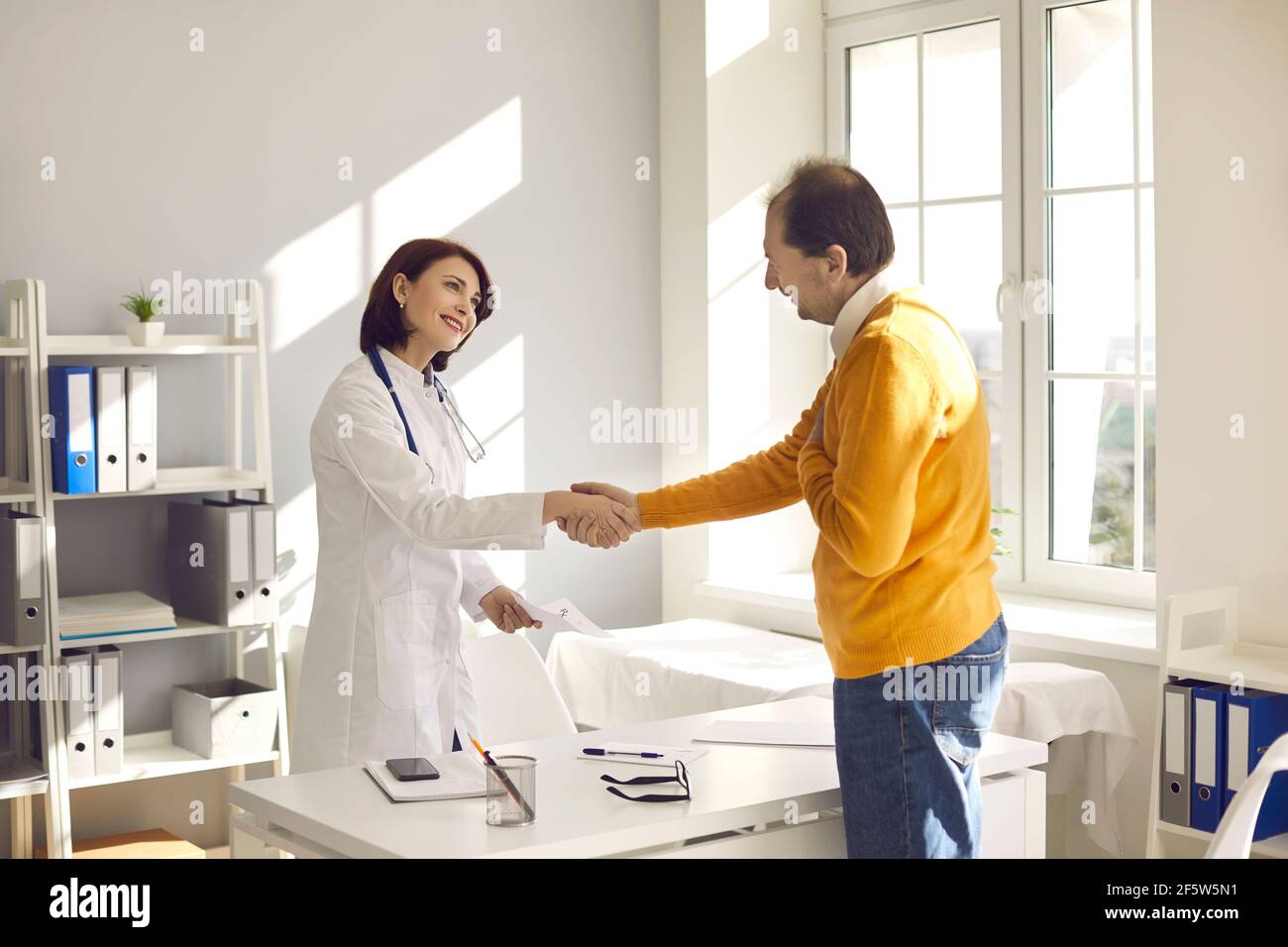 Paziente maschile sano di mezza età ringraziando il medico femminile scuotendola mano Foto Stock