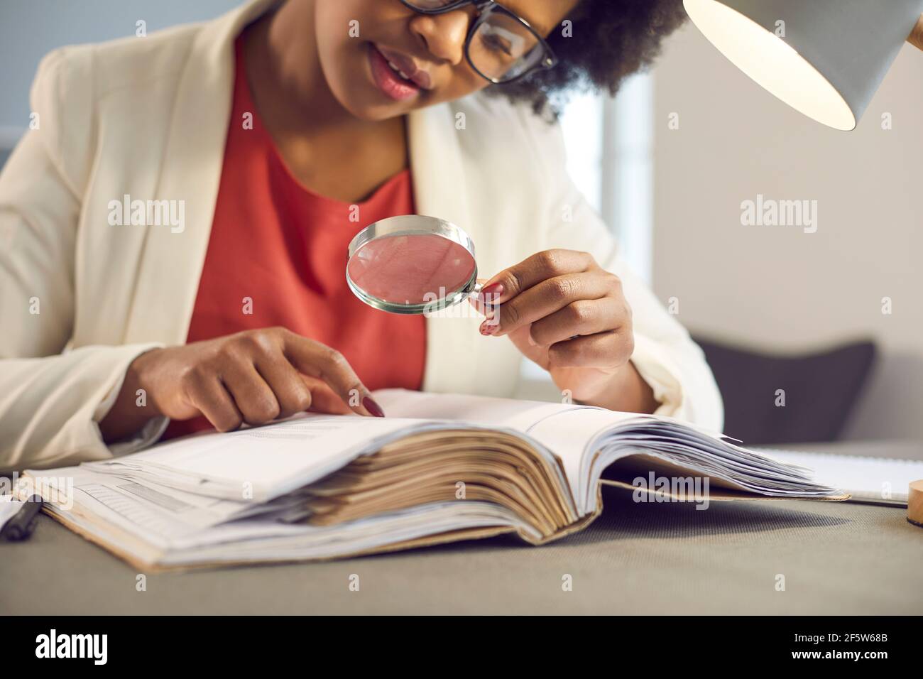 Giovane donna afro-americana Bbusiness leggere guardando attraverso la lente d'ingrandimento Foto Stock