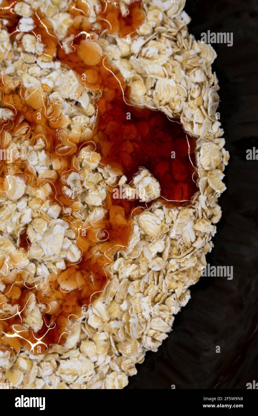 fiocchi d'avena in un piatto nero gocciolato con sciroppo o. miele Foto Stock