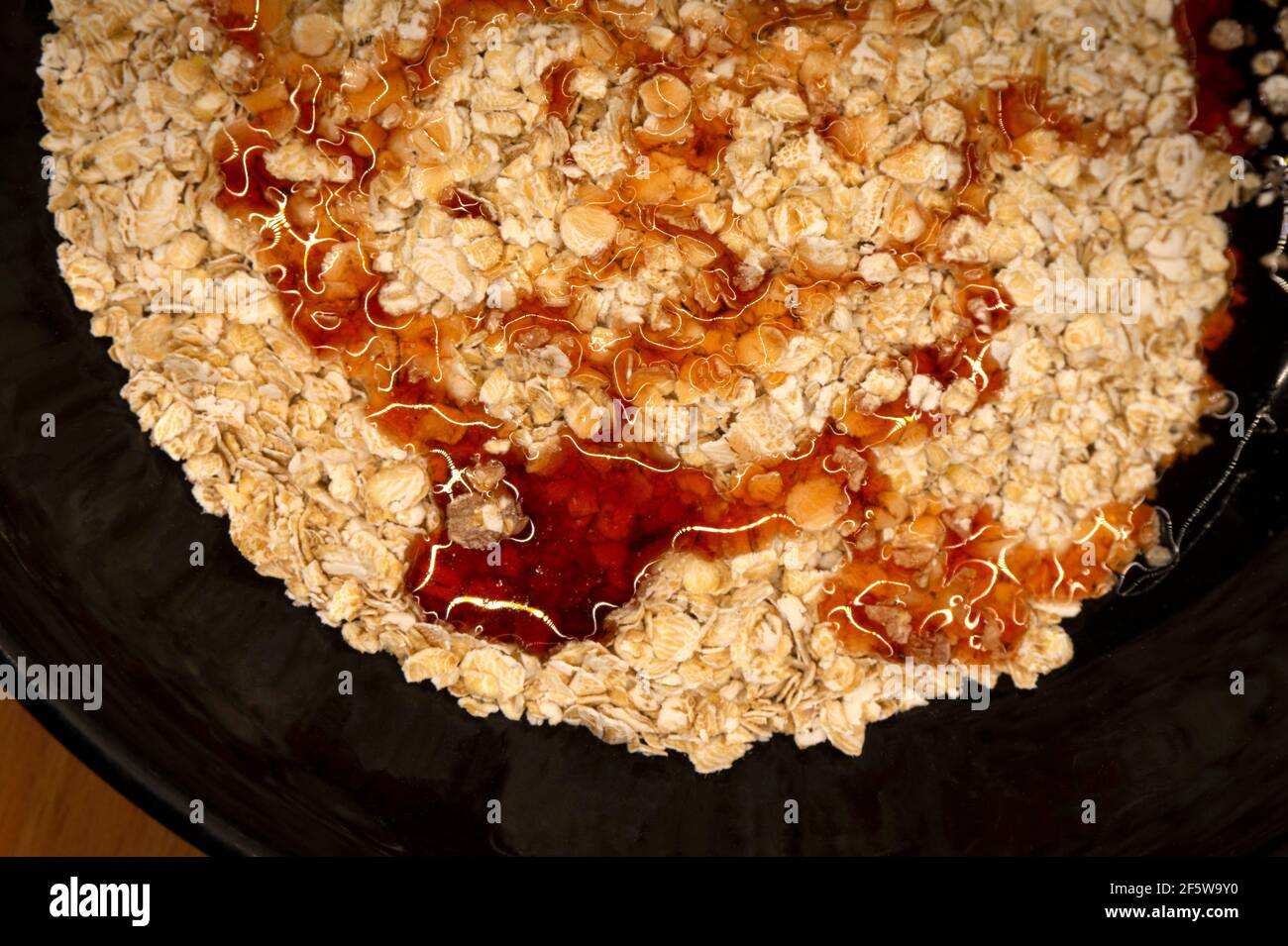 fiocchi d'avena in un piatto nero gocciolato con sciroppo o. miele Foto Stock