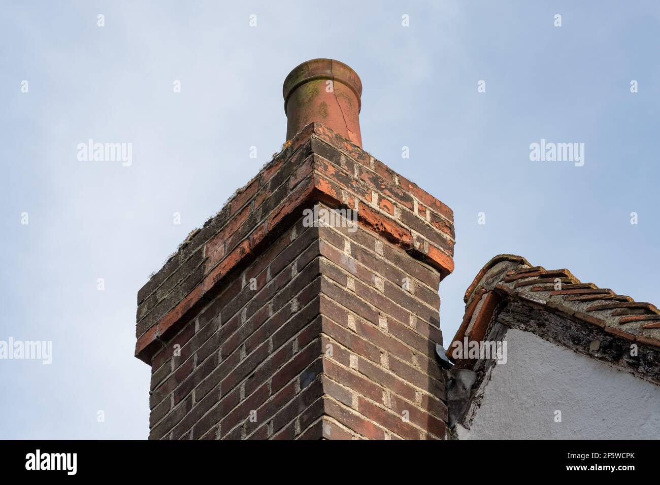 Vista dettagliata di un camino e camino costruito in mattoni pesantemente intemperie e cracking. La pentola mostra il segno di rottura e la muratura è stata alterata. Foto Stock