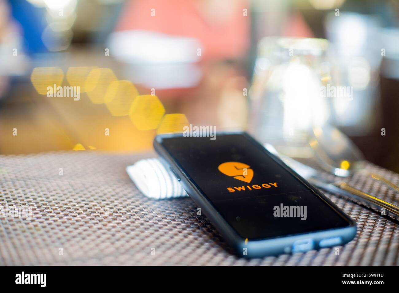 maschera in tessuto blu con telefono cellulare a lato con un logo swiggy nel ristorante che mostra la popolarità per mangiare sicuro fuori e ordinando dentro come coronavirus Foto Stock