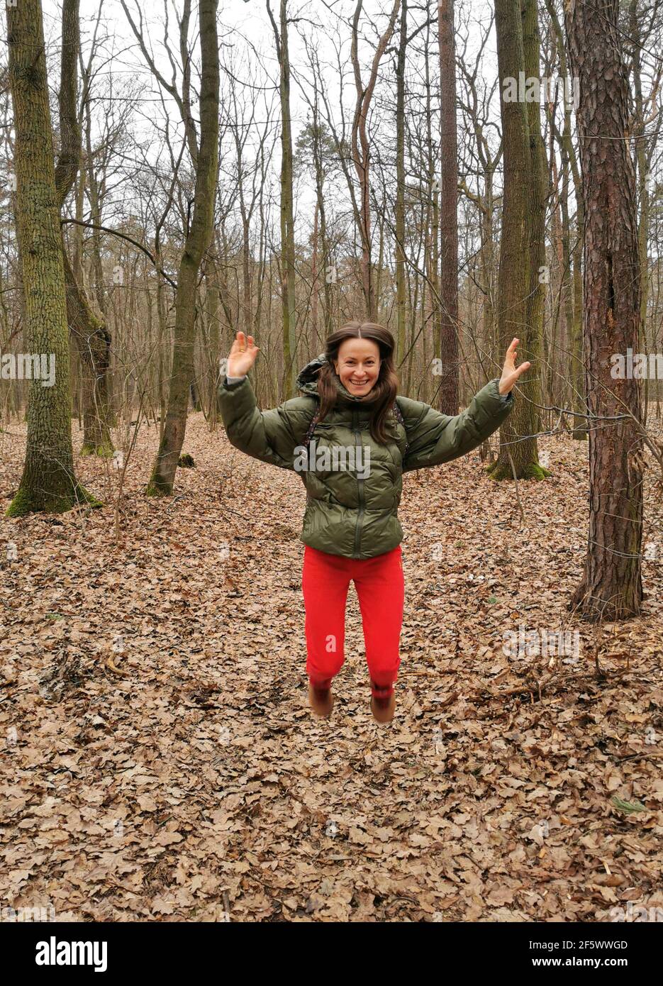 Sorridente, felice e positiva ragazza nel parco tra gli alberi gode di vita. Una donna in un vestito sportivo, salta in su, si sta esercitando all'aperto Foto Stock