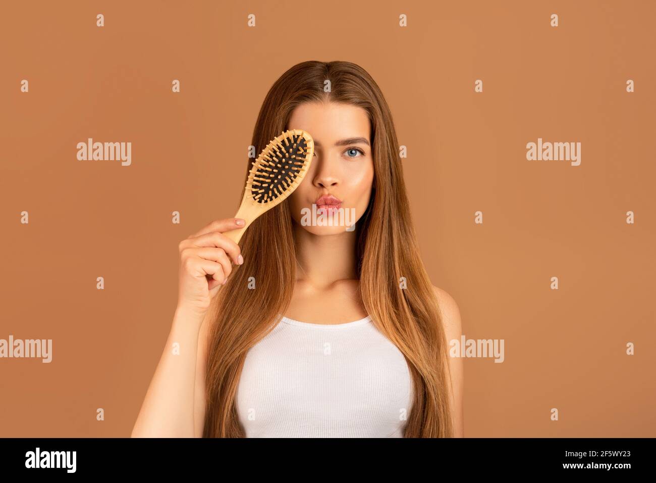 Cosmetici naturali per capelli setosi. Ritratto di bella giovane donna che tiene il pennello vicino al suo occhio su sfondo marrone Foto Stock