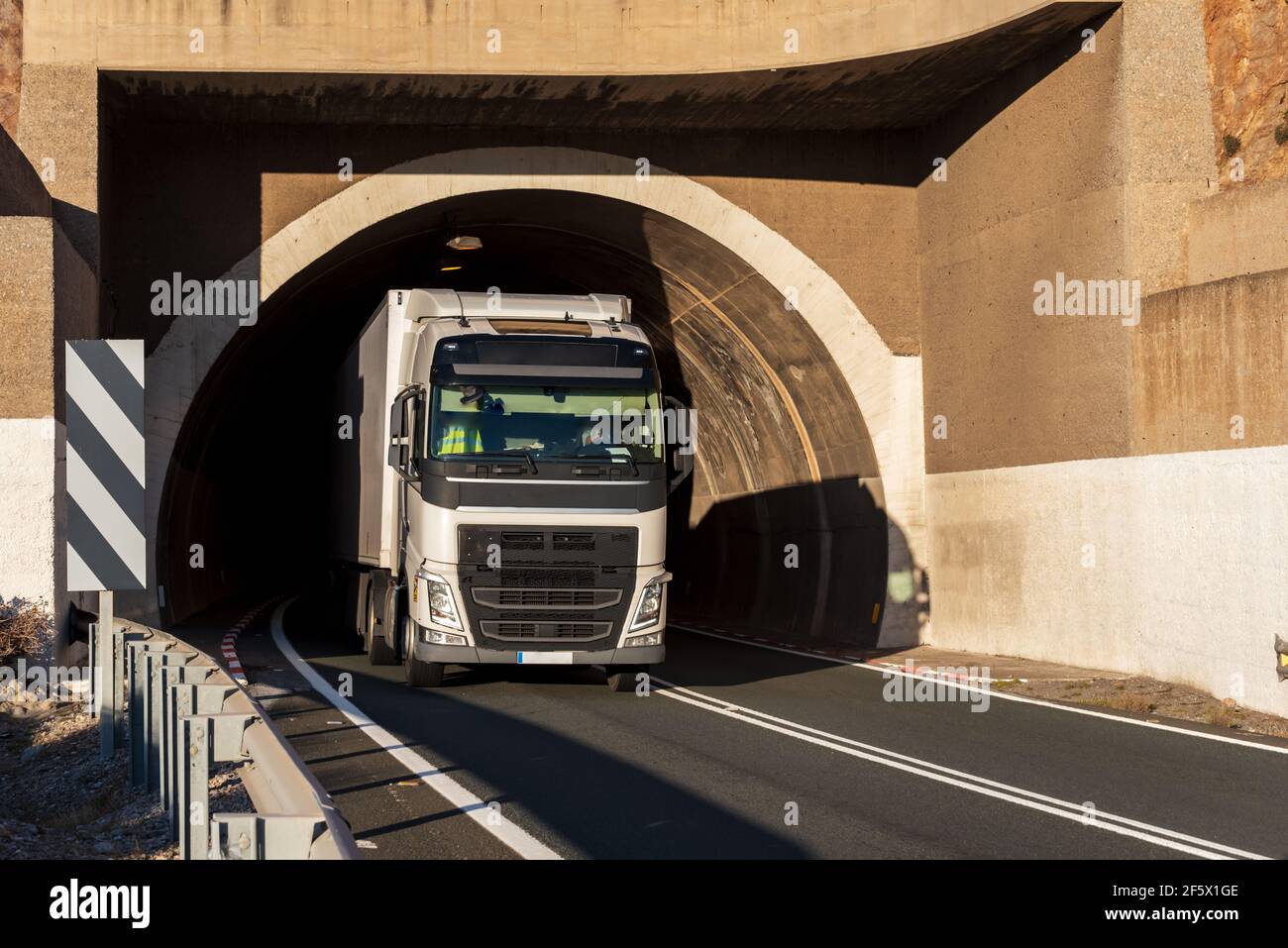 Autocarro con semirimorchio refrigerato che lascia il tunnel di una strada convenzionale, con traffico a due vie. Foto Stock