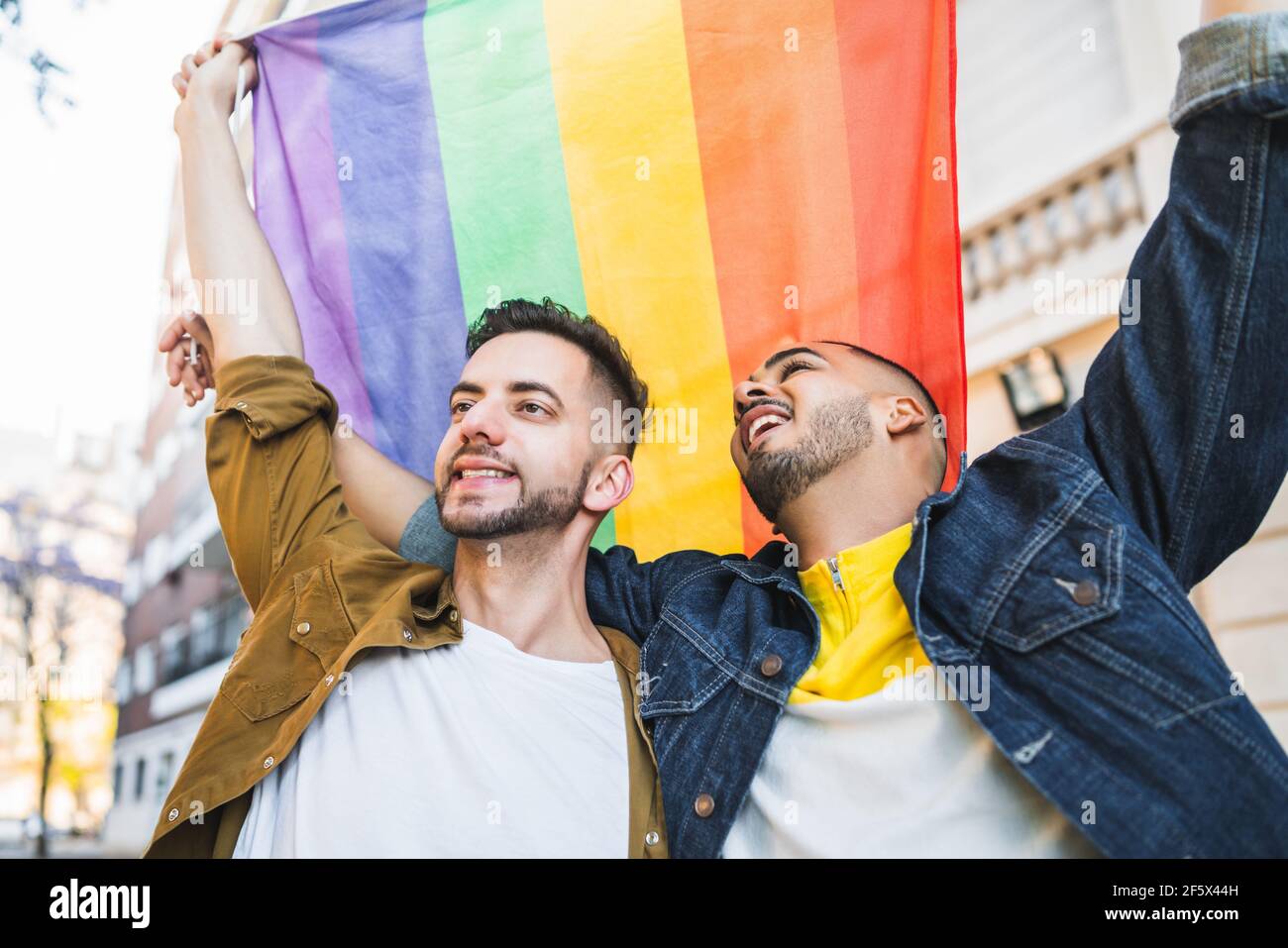 Coppia gay abbracciando e mostrando il loro amore con bandiera arcobaleno. Foto Stock