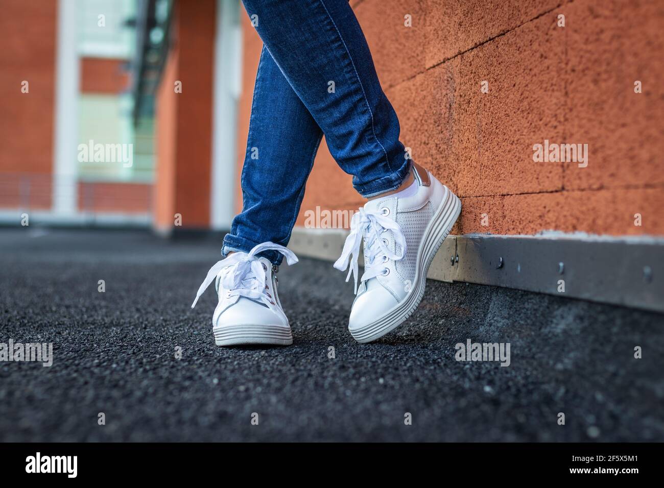Donna con sneaker bianche in pelle a parete pendente in città, vista  ravvicinata sulle gambe femminili che indossano jeans e scarpe sportive.  Concetto di moda Foto stock - Alamy