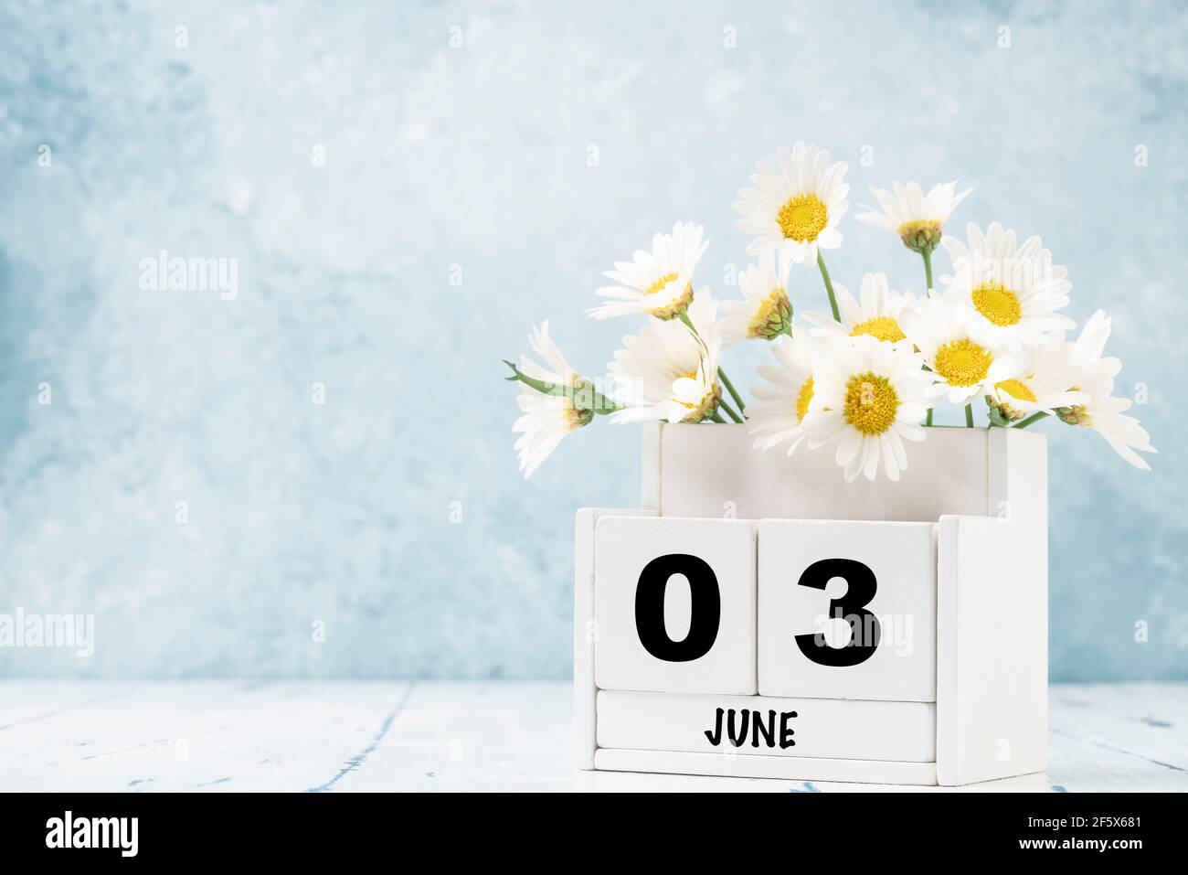 Calendario cubico bianco per giugno decorato con fiori margherita sopra sfondo blu con spazio per la copia Foto Stock