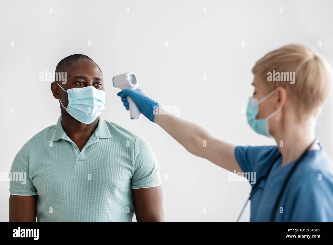Donna di mezza età in maschera protettiva, guanti e misura la temperatura uniforme con il moderno termometro a infrarossi Foto Stock