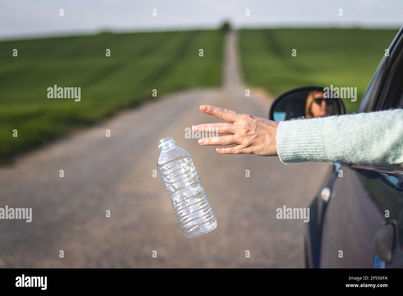 Il conducente getta via la bottiglia di plastica dal finestrino dell'auto su strada. Conservazione ambientale. Concetto di inquinamento plastico Foto Stock