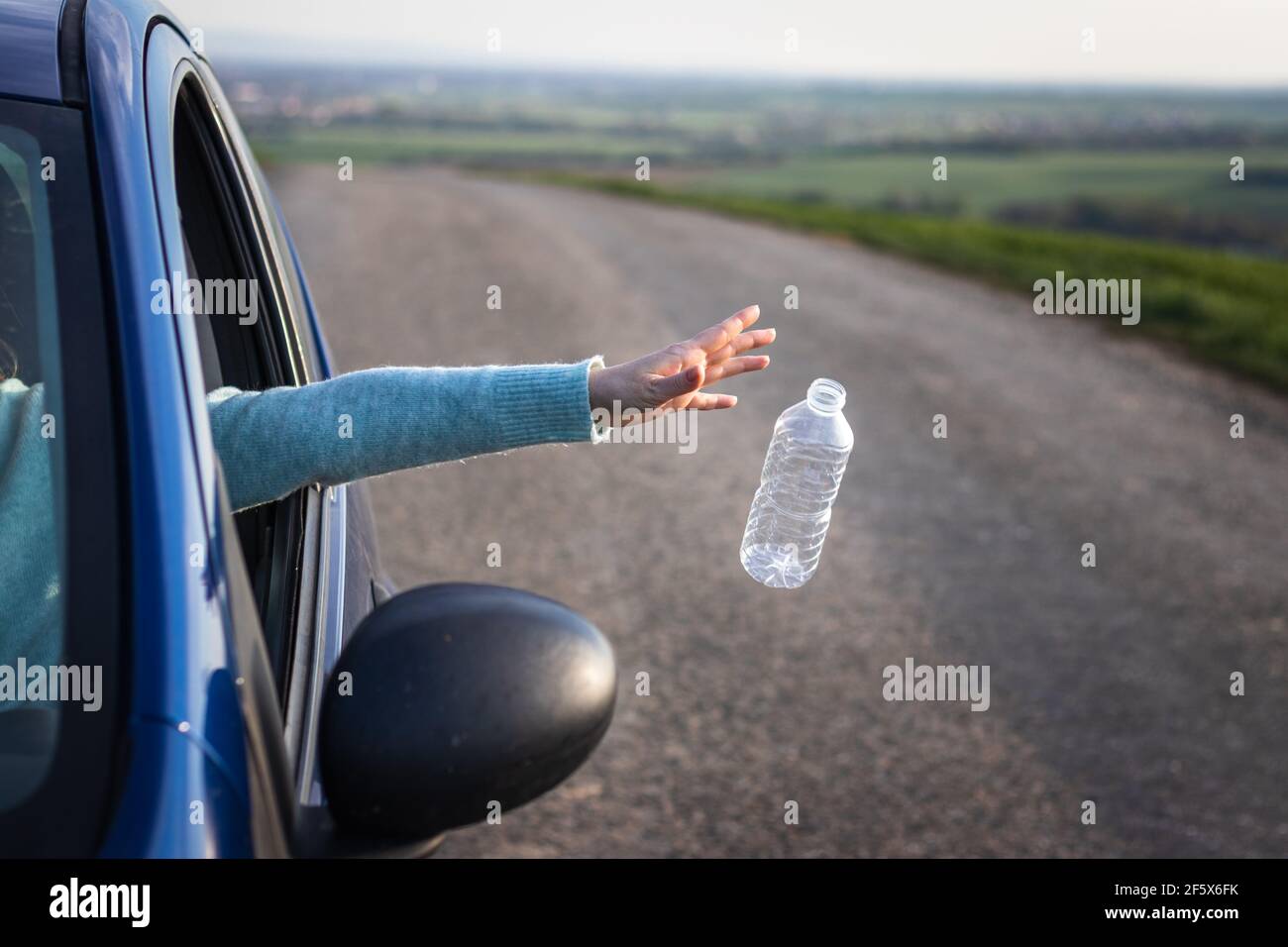 Non inquinare la natura con i rifiuti di plastica! Il conducente getta via la bottiglia di plastica dal finestrino dell'auto. Conservazione ambientale Foto Stock