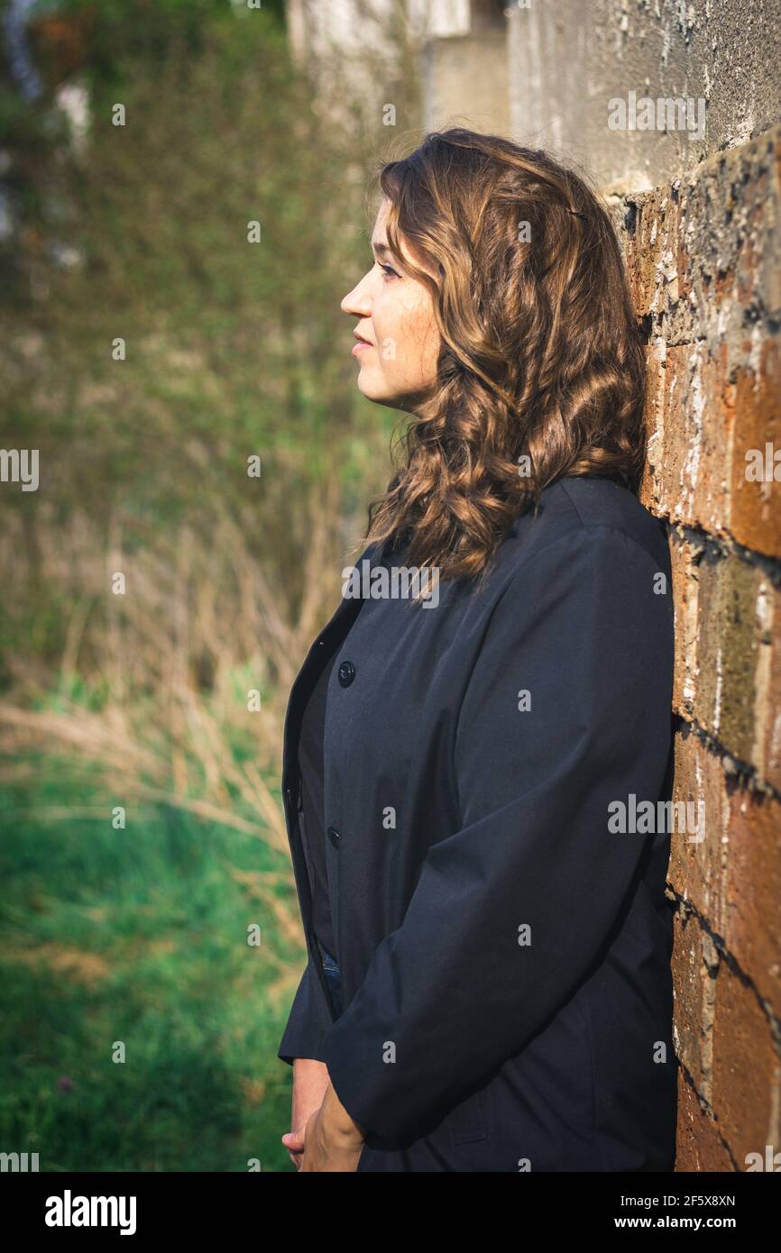 Ritratto di bella marrone capelli giovane donna pendente muro. Elegante donna caucasica con giacca nera Foto Stock