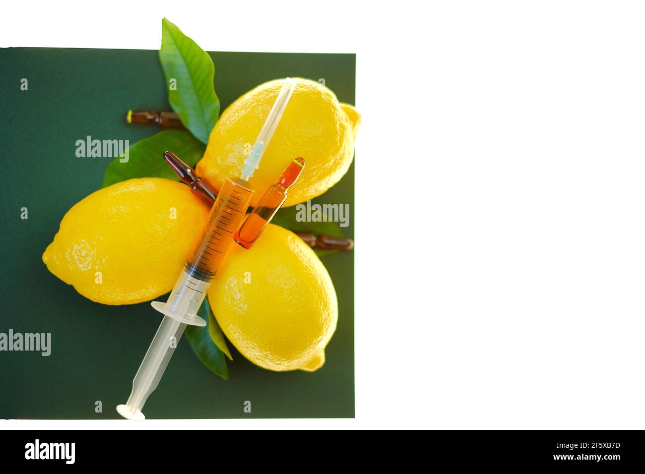 Siero di vitamina C. con vitamina C. ampolle di vetro da vicino, siringa con soluzione iniettabile e limoni di frutta su fondo verde, isolati su fondo bianco Foto Stock