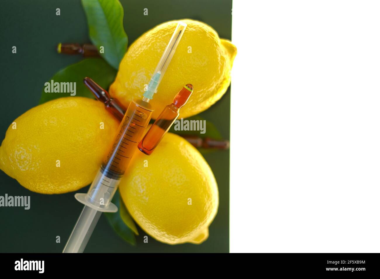 Siero di vitamina C. con vitamina C. ampolle di vetro da vicino, siringa con soluzione iniettabile e limoni di frutta su fondo verde, isolati su fondo bianco Foto Stock