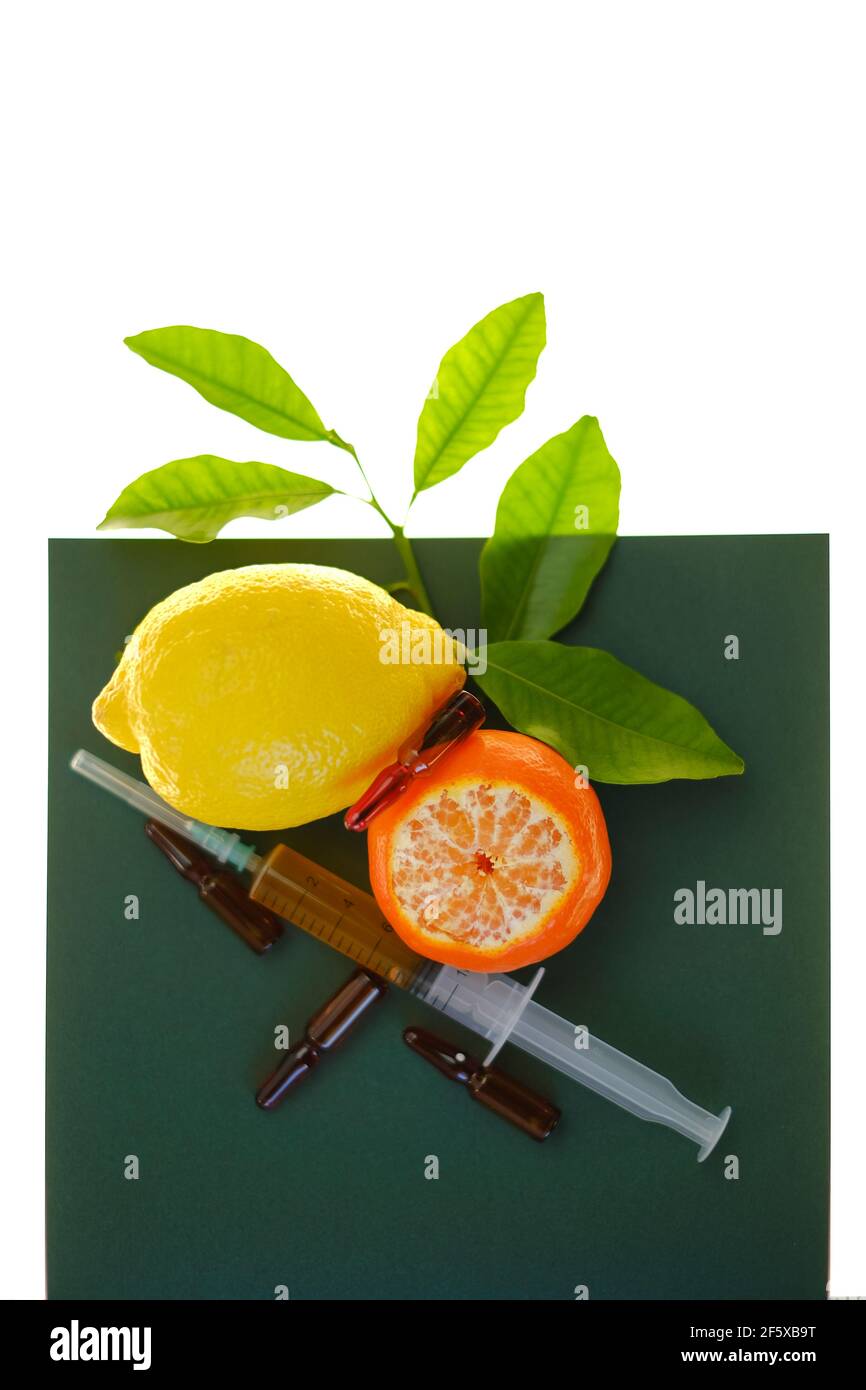 Siero di vitamina C. con vitamina C. ampolle di vetro da vicino, siringa con soluzione iniettabile e limoni di frutta su fondo verde su fondo bianco Foto Stock