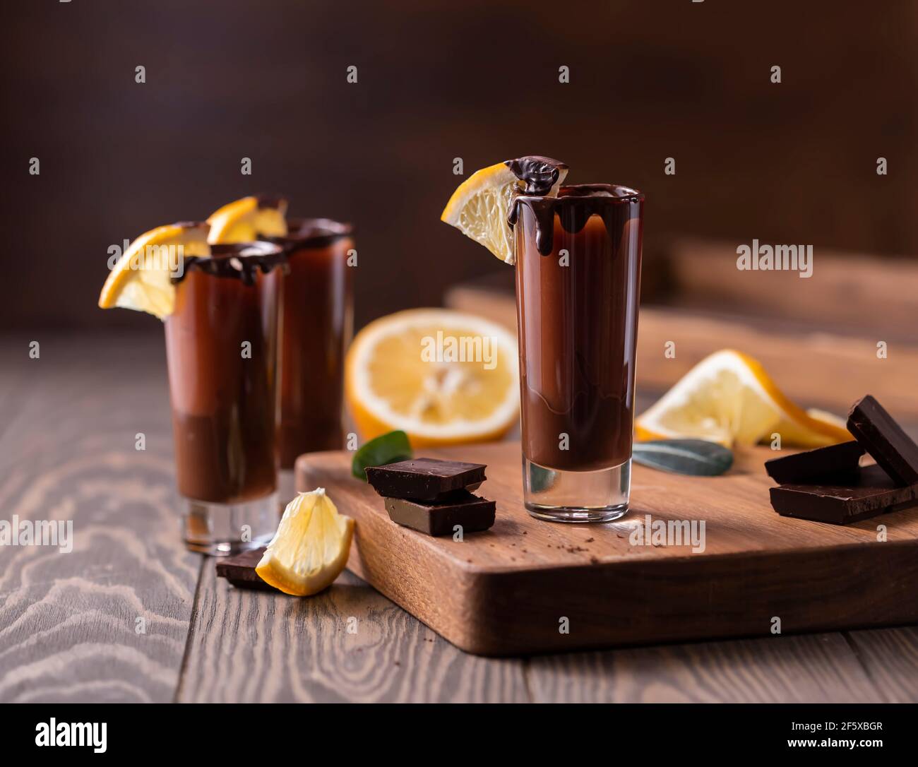 Cocktail in bicchierino con cioccolato, liquore alla crema, arance fresche su sfondo scuro. Festa fatta in casa con bevande a base di shot. Menu bar, ricette. Primo piano, selec Foto Stock