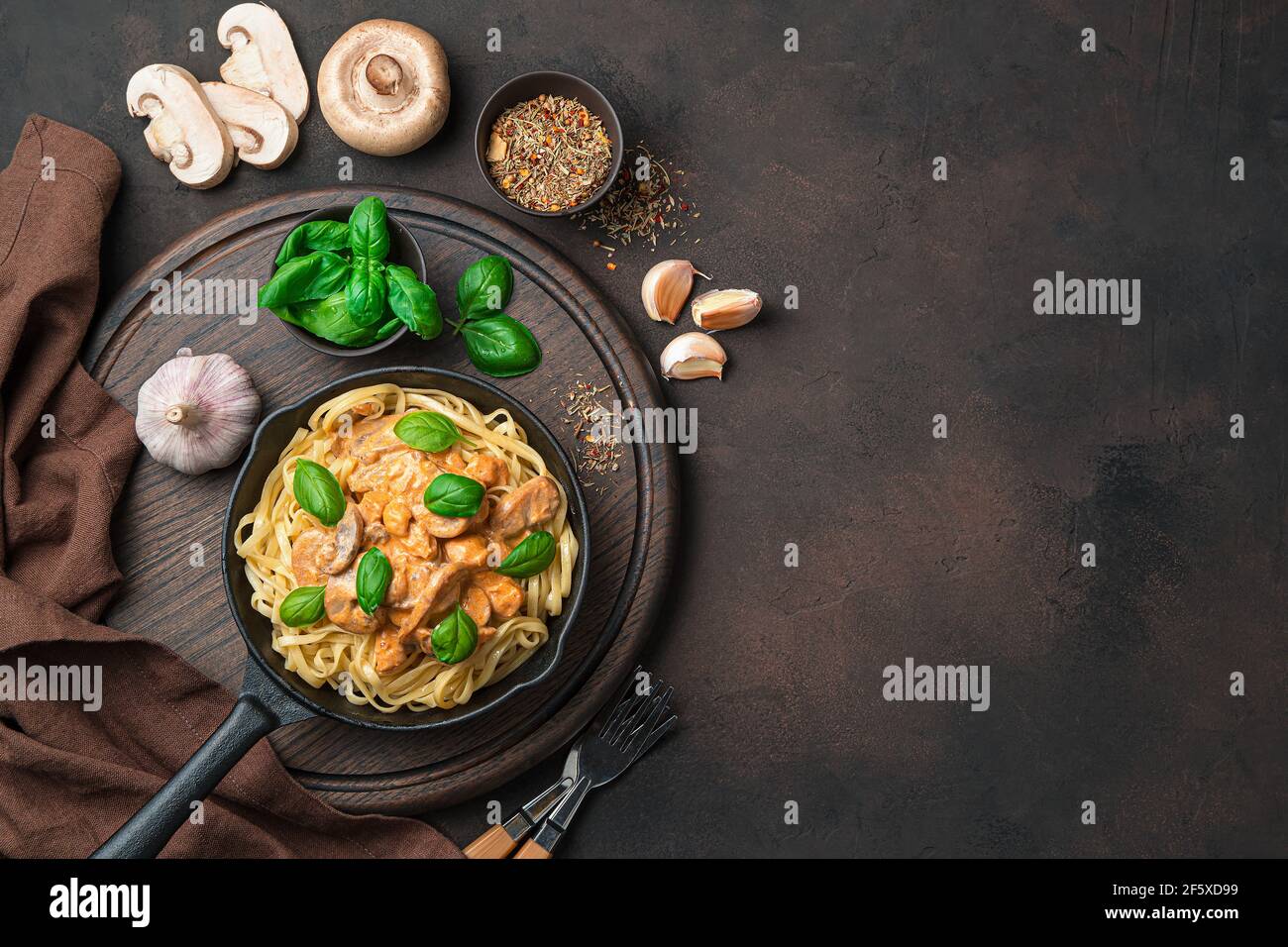 Sfondo culinario con pasta e salsa cremosa di funghi, basilico, aglio e spezie su sfondo marrone scuro. Foto Stock