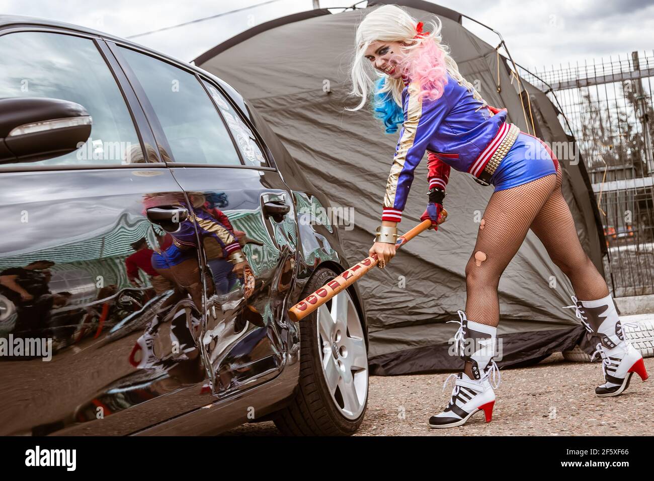 Mosca, Russia - 06 luglio 2020: Harley Quinn colpisce una macchina nera parcheggiata con una mazza da baseball. C'è un'ammaccatura nella vettura, la vettura è danneggiata. Cosplay, ragazza vestita come costume di carattere Foto Stock