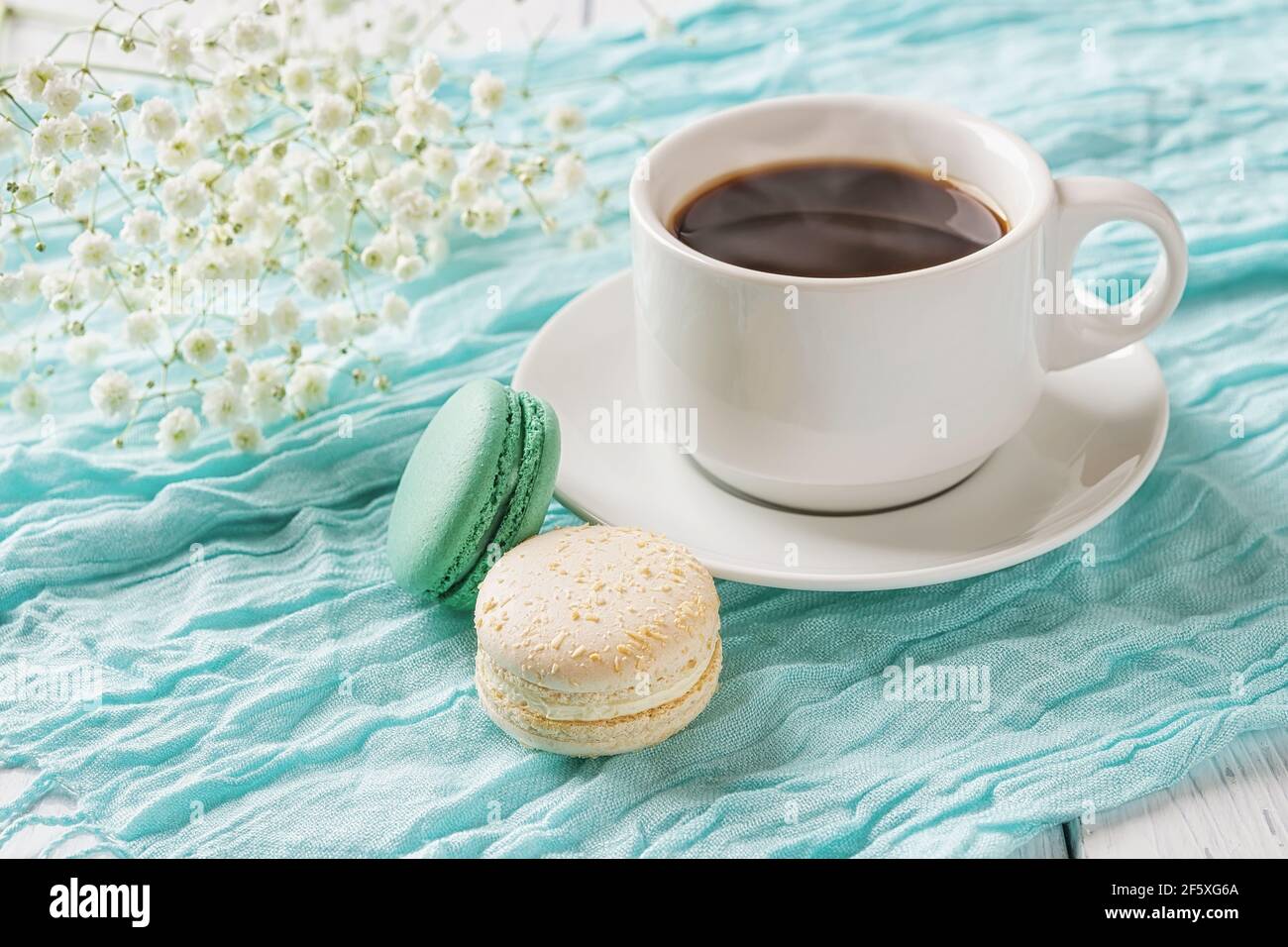 Tazza di caffè caldo e due amaretti su fondo di tessuto turchese. Colazione dolce con deliziosi biscotti alla meringa di mandorle. Macaroni colorati. Foto Stock