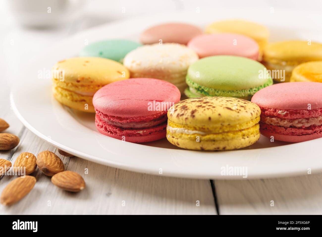 Primo piano di gustosi macaroni multicolore su un piatto di porcellana bianca. Colazione dolce con deliziosi biscotti alla meringa di mandorle. Torte di macaron colorate. Foto Stock