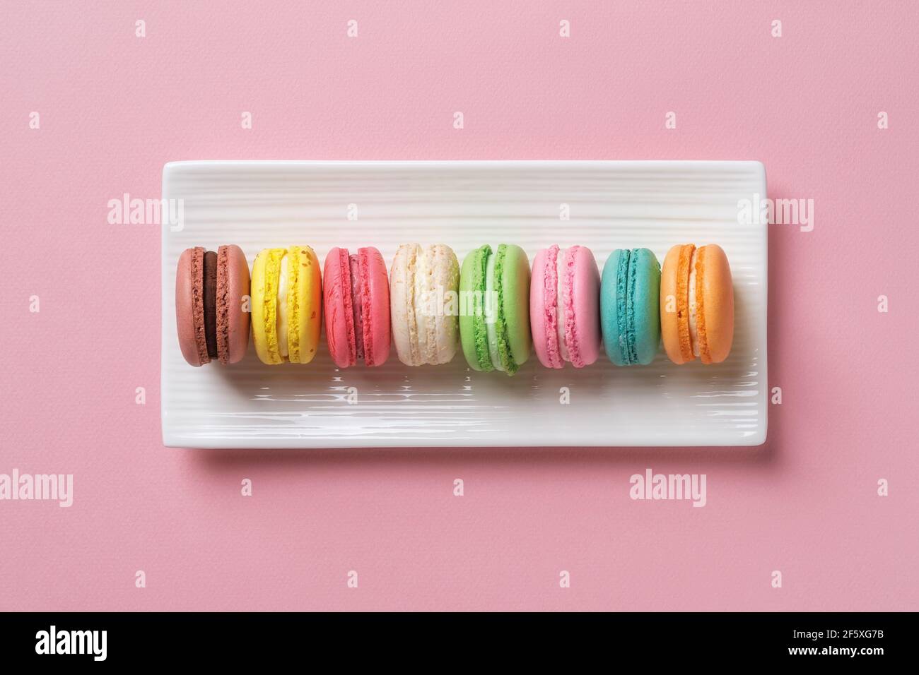 Macaroni multicolore su una piastra di ceramica rettangolare bianca su sfondo rosa pastello. Colazione dolce con deliziosi biscotti alla meringa di mandorle. Foto Stock