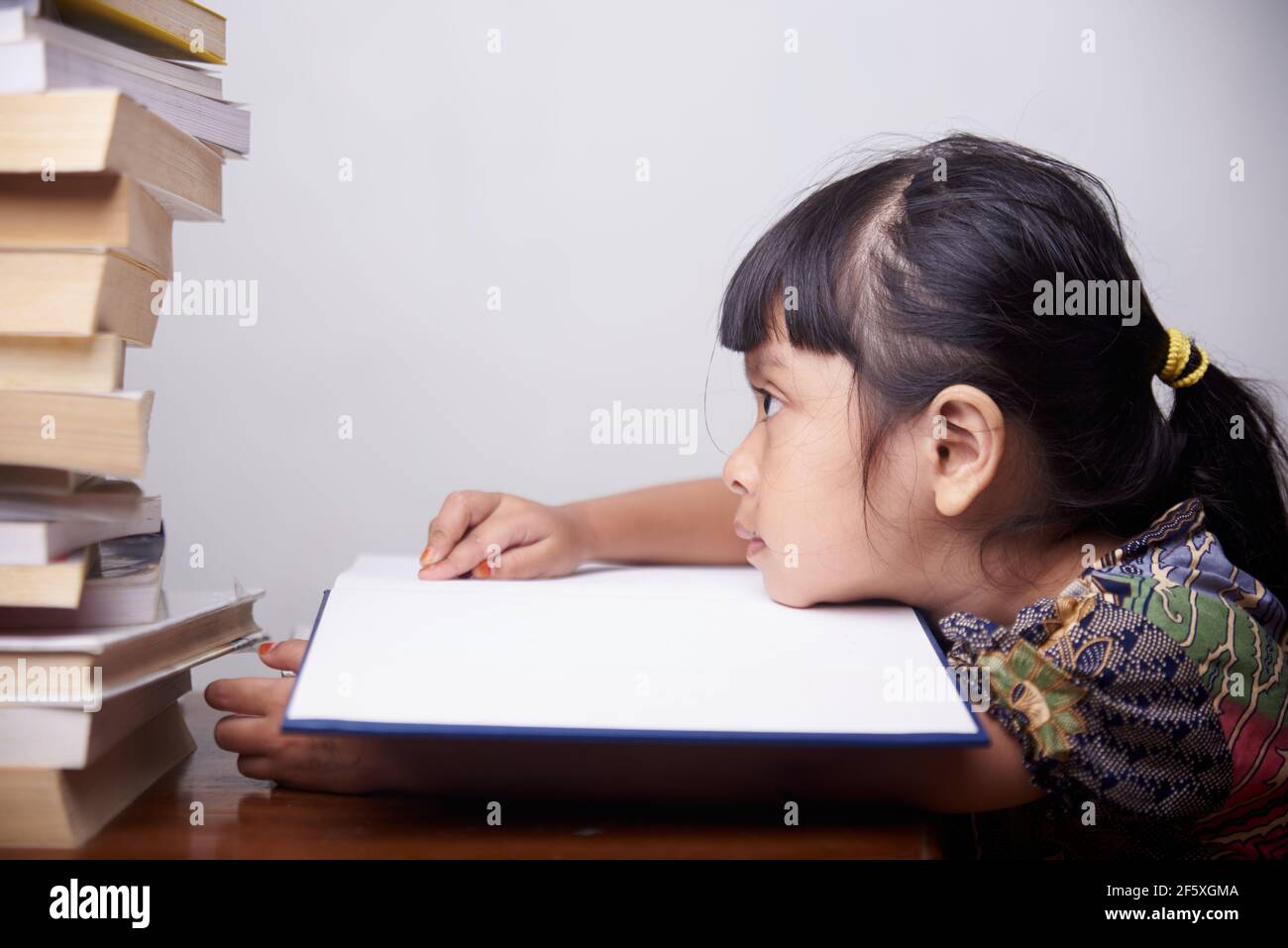 Bambina annoiata con una pila di libri a casa Foto Stock