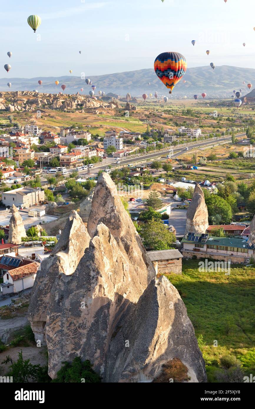 Paesaggio soleggiato della città di Goreme con decine di palloncini che volano nel cielo della Cappadocia all'alba nella Turchia centrale. Foto Stock