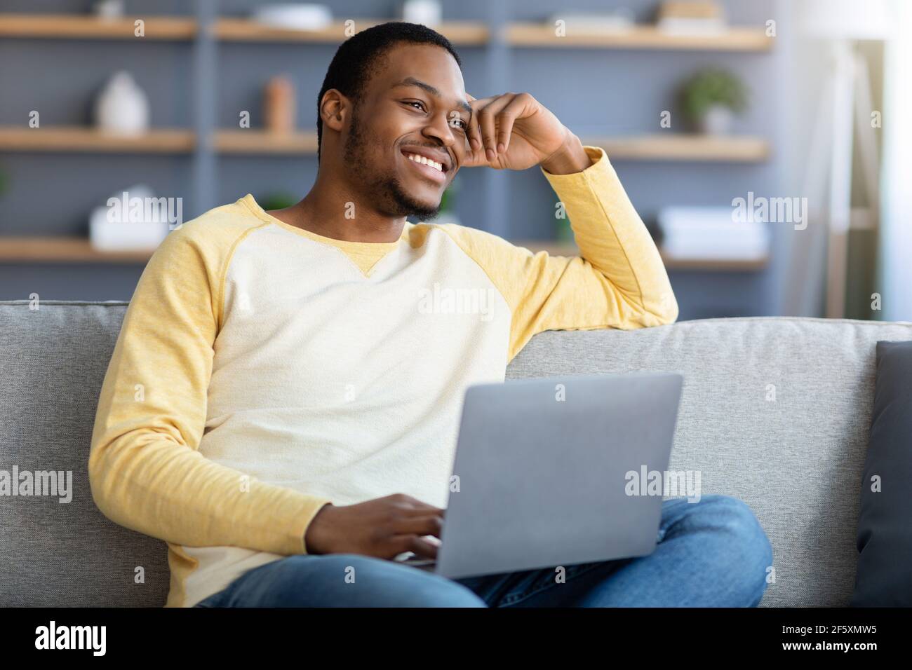 buon ragazzo afroamericano che si gode il fine settimana a casa, utilizzando il computer portatile Foto Stock