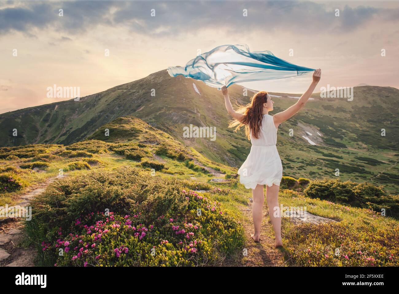 La donna sente la libertà e gode della natura in montagna con tessuto blu in mani al tramonto Foto Stock