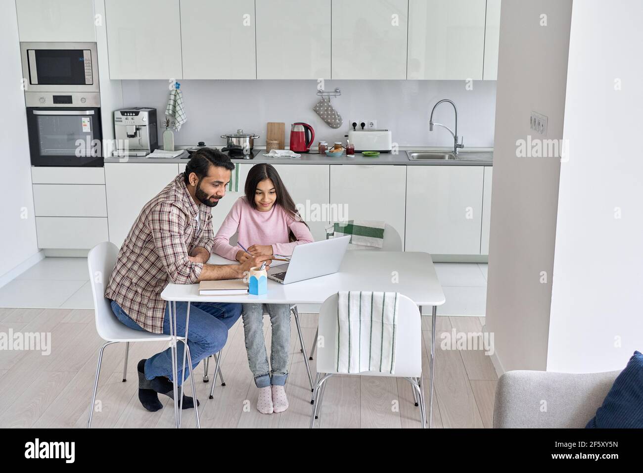 Felice giovane padre indiano genitore aiutare la figlia adolescente imparare a casa. Foto Stock