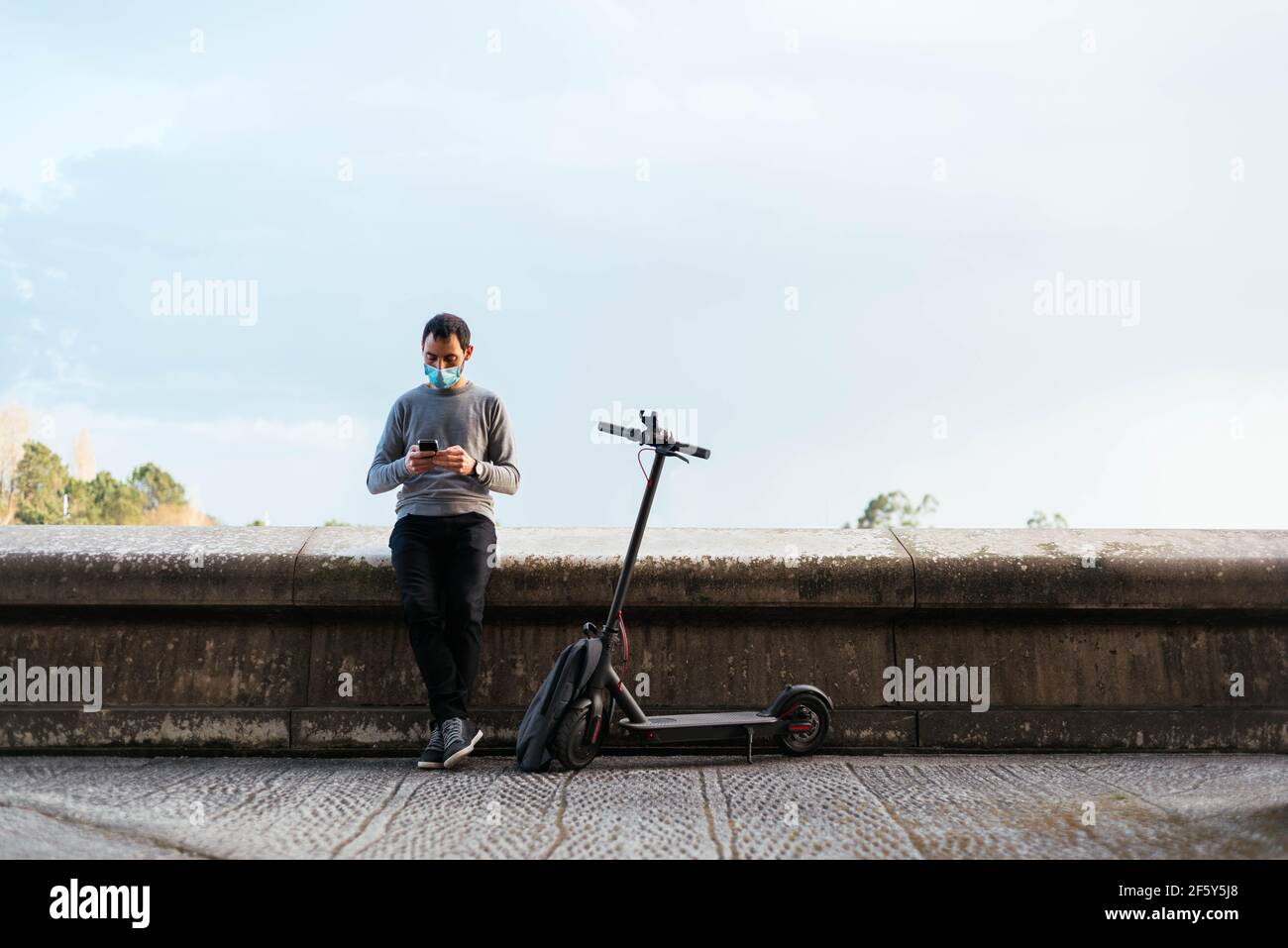 Uomo che usa lo smartphone vicino a uno scooter elettrico Foto Stock