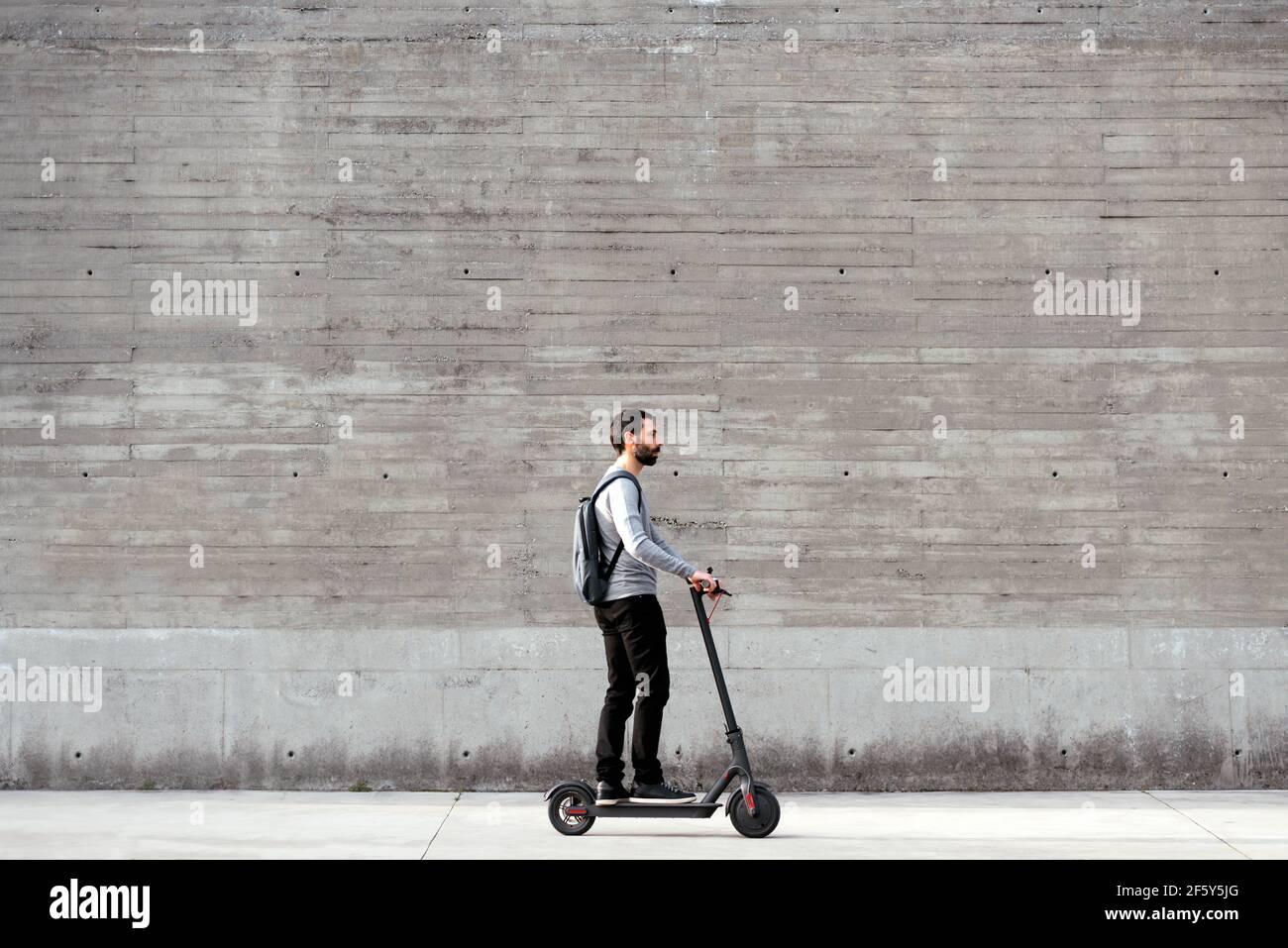 Uomo che guida uno scooter elettrico di fronte alla parete grigia Foto Stock