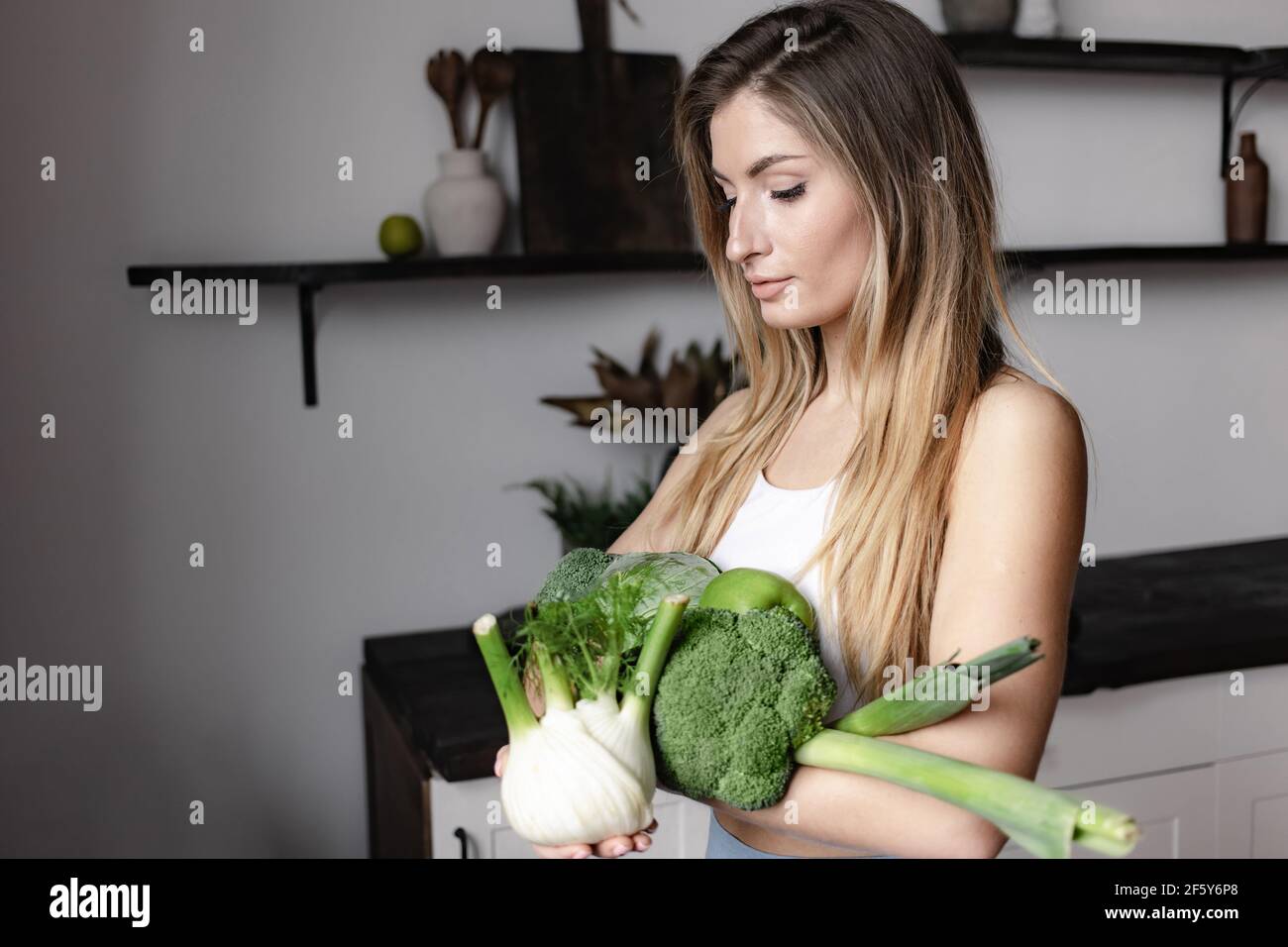 Una donna di idoneità tiene un pieno di verdure verdi grezze fresche- finocchi, broccoli, avocado, mela, porro, cavolo. Disintossicare sano cibo vegano dieta. Foto Stock