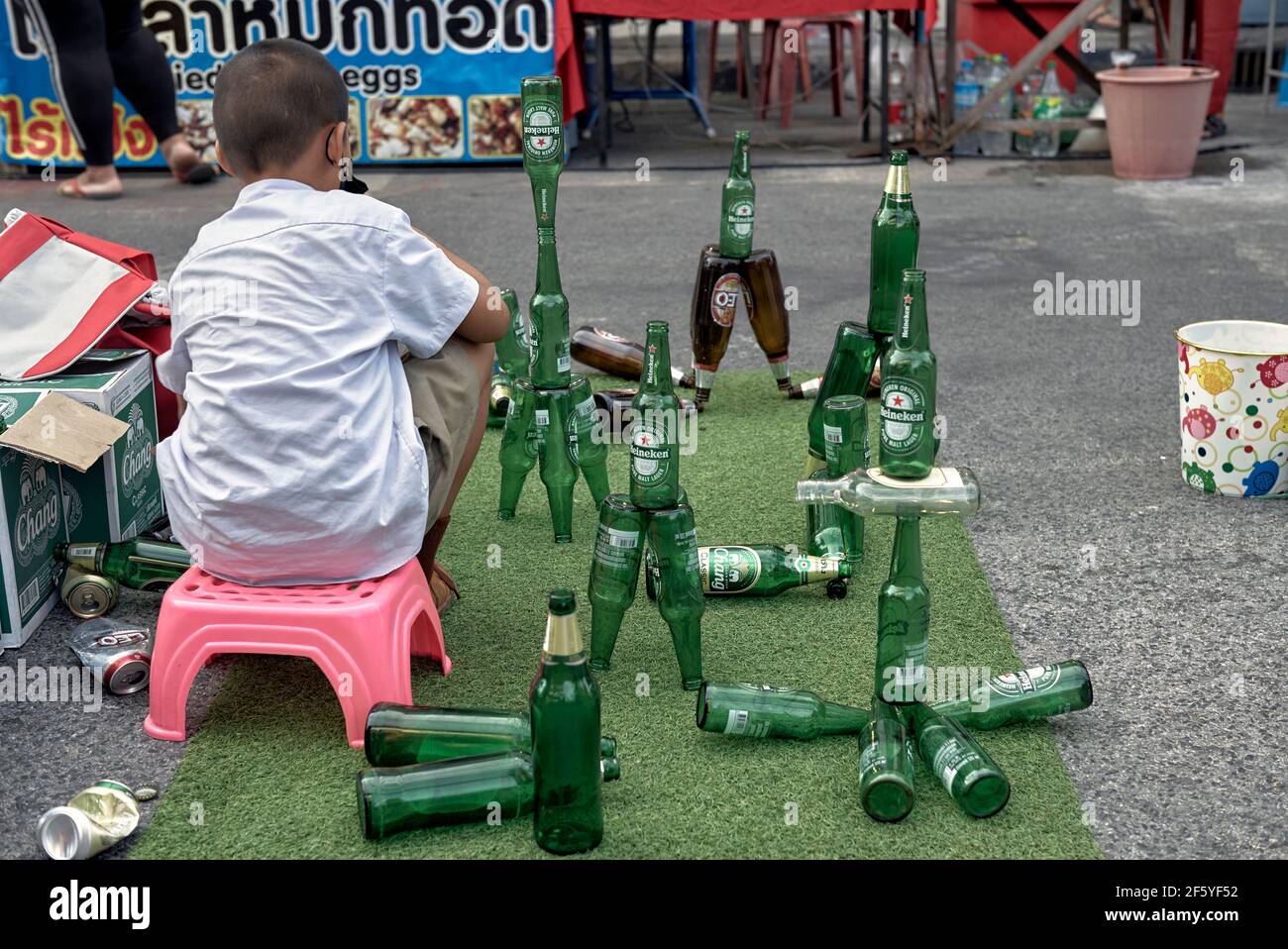 Bambino fantasioso. Ragazzo giovane che organizza e bilancia le bottiglie di birra trucco per guadagnare soldi sulla strada. Thailandia, Sud-est asiatico Foto Stock