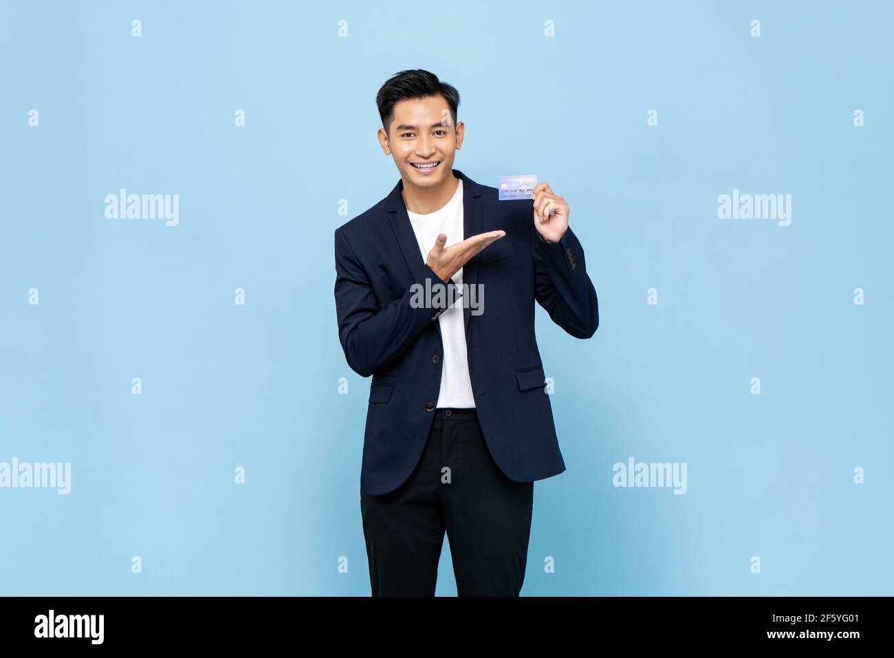 Bell'uomo asiatico sorridente in costume semi formale mostrando credito scheda in blu chiaro isolato sfondo studio Foto Stock