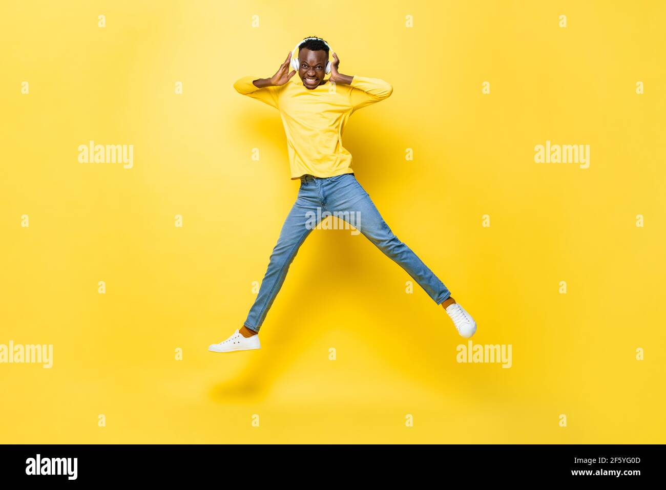 Felice giovane africano uomo che indossa le cuffie ascoltare la musica e. salto in giallo isolato studio sfondo Foto Stock