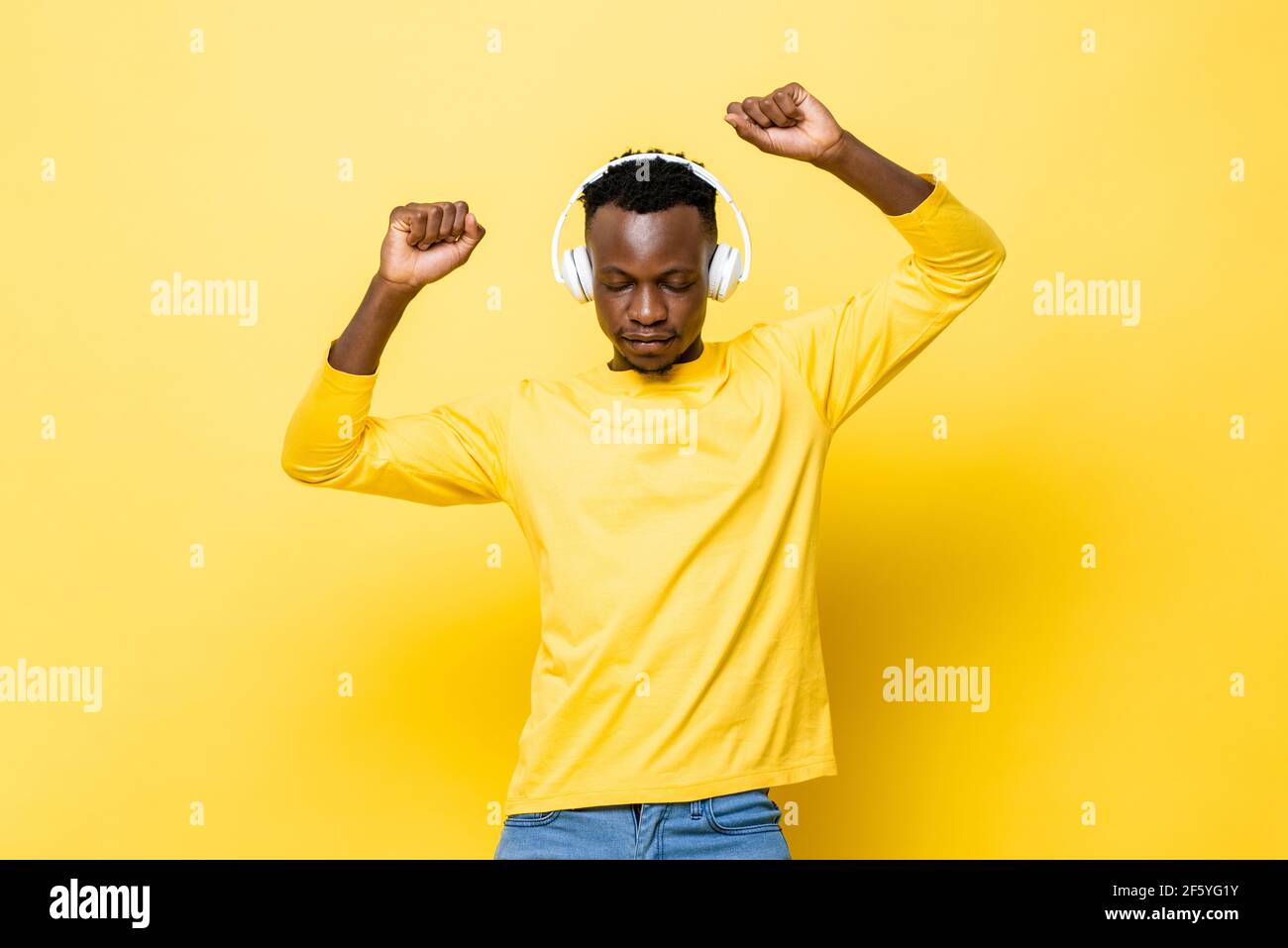 Giovane africano che ascolta la musica con le cuffie che chiudono gli occhi e danzare su sfondo giallo dello studio Foto Stock