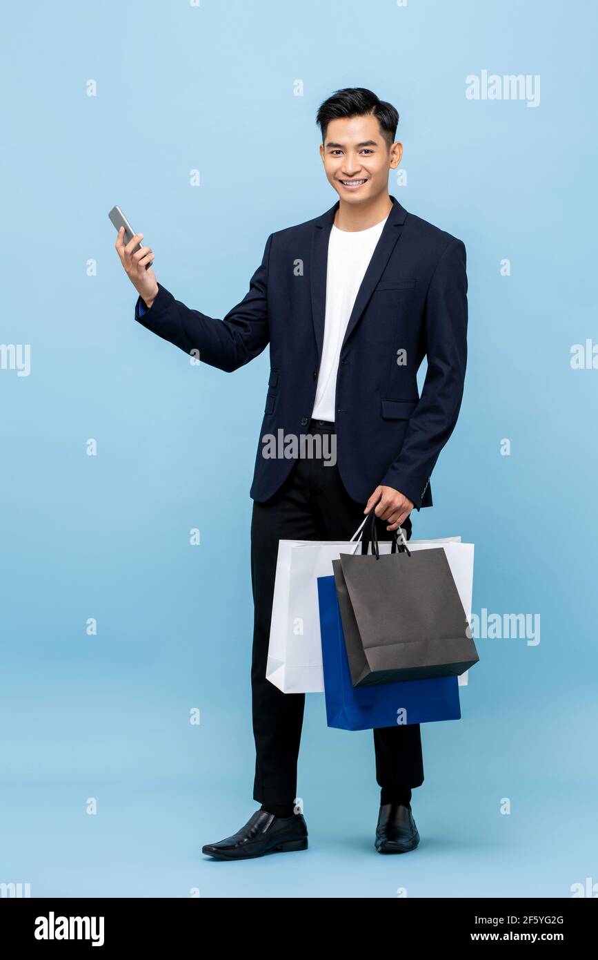 Giovane bell'uomo del sud-est asiatico che tiene il telefono cellulare e lo shopping borse in blu chiaro studio isolato sfondo Foto Stock