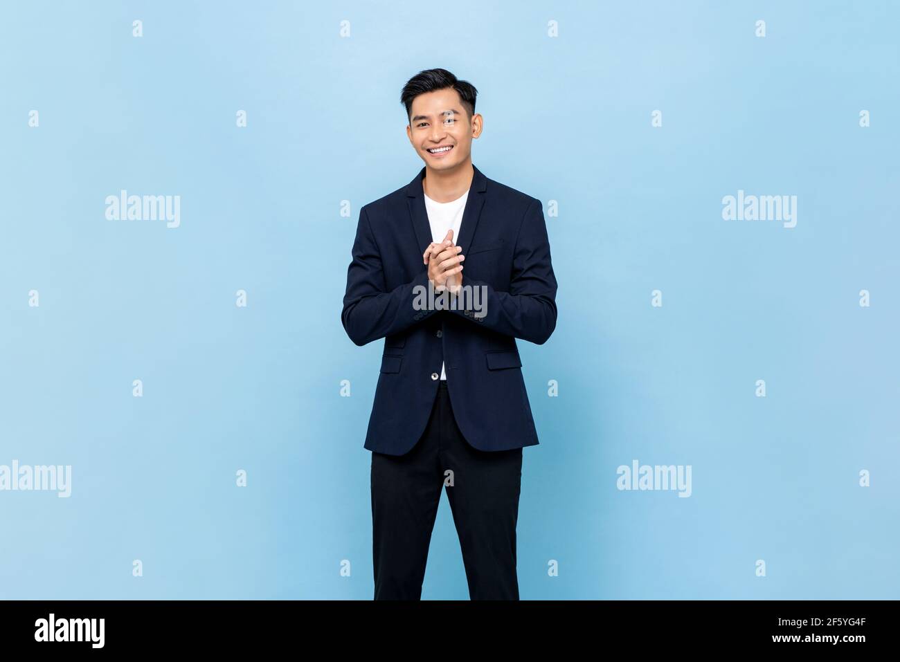 Sorridente giovane bell'uomo del sud-est asiatico aggrappando le mani in modo impressionante sfondo isolato dello studio azzurro Foto Stock