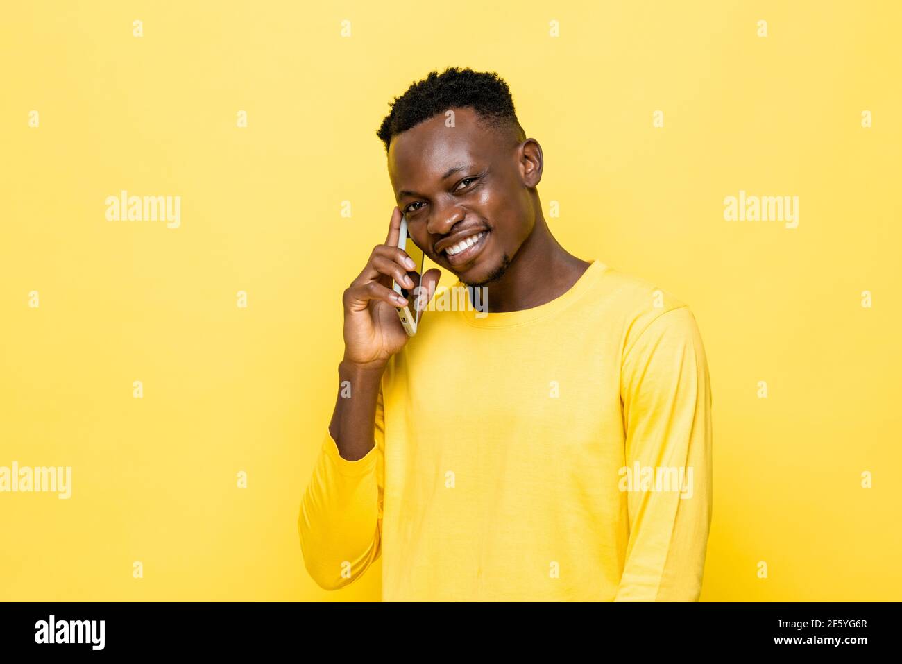 Sorridente giovane africano che parla sul cellulare in giallo sfondo di studio isolato Foto Stock